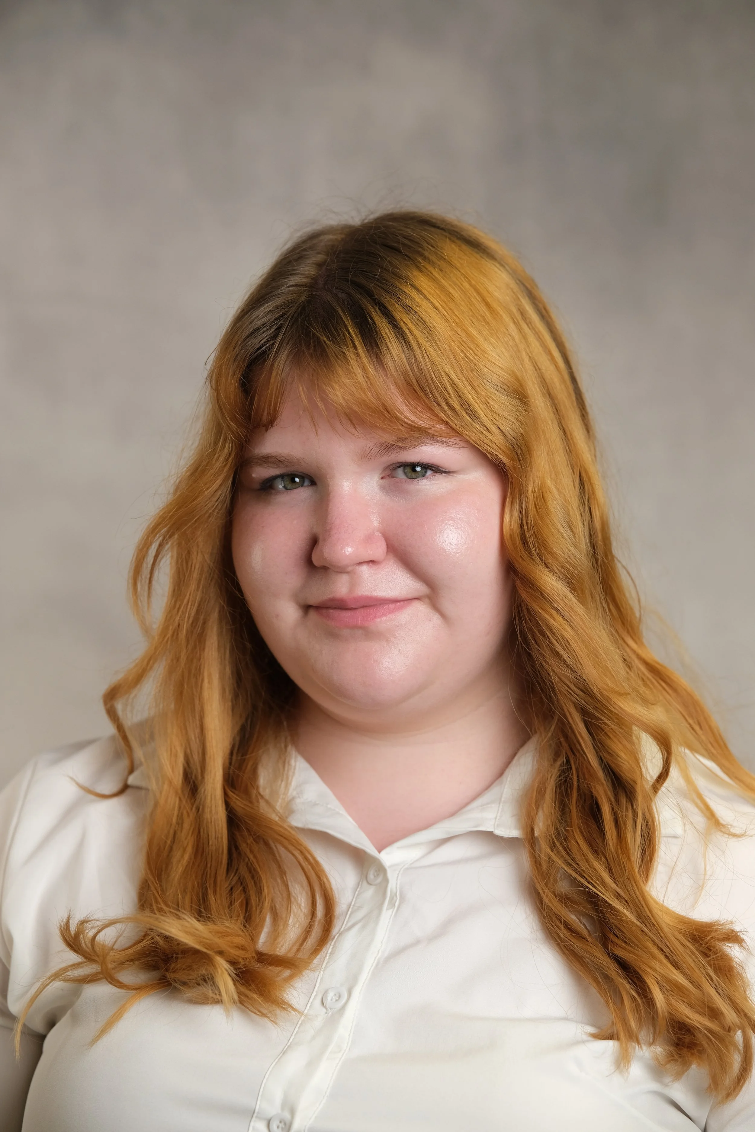 Portrait of a woman with red hair and light skin, wearing a white shirt, against a neutral background.