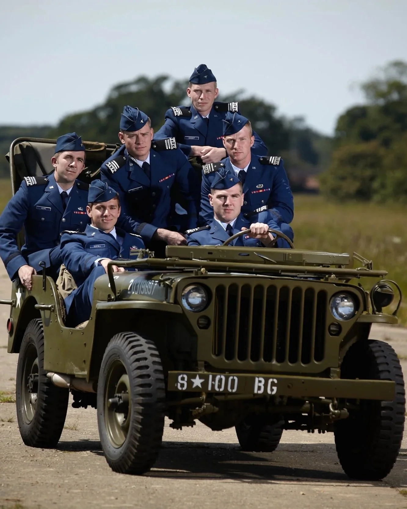 Group of soldiers in blue uniforms riding in a military jeep outdoors.