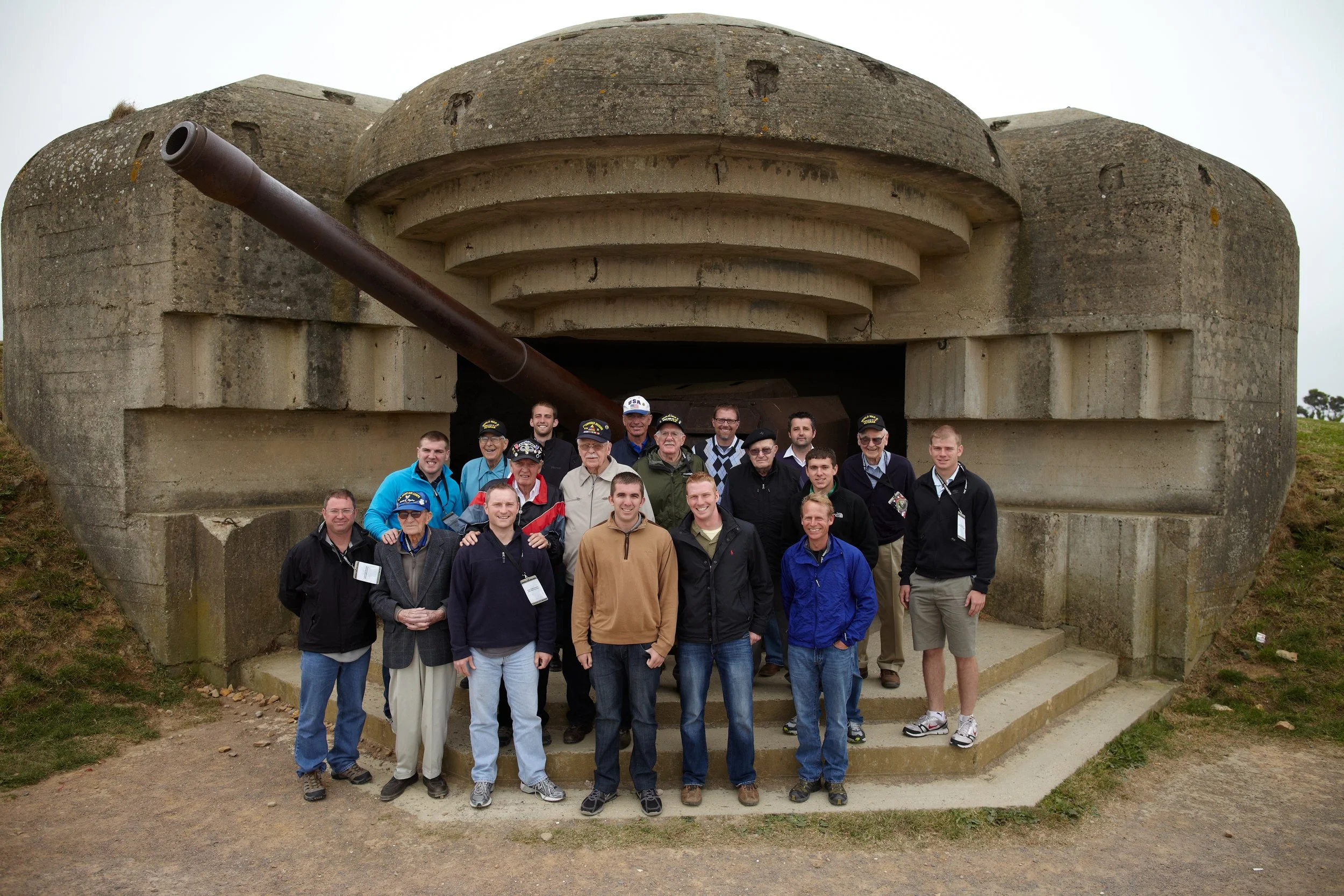 Group of people standing in front of a World War II bunker with a large artillery cannon.