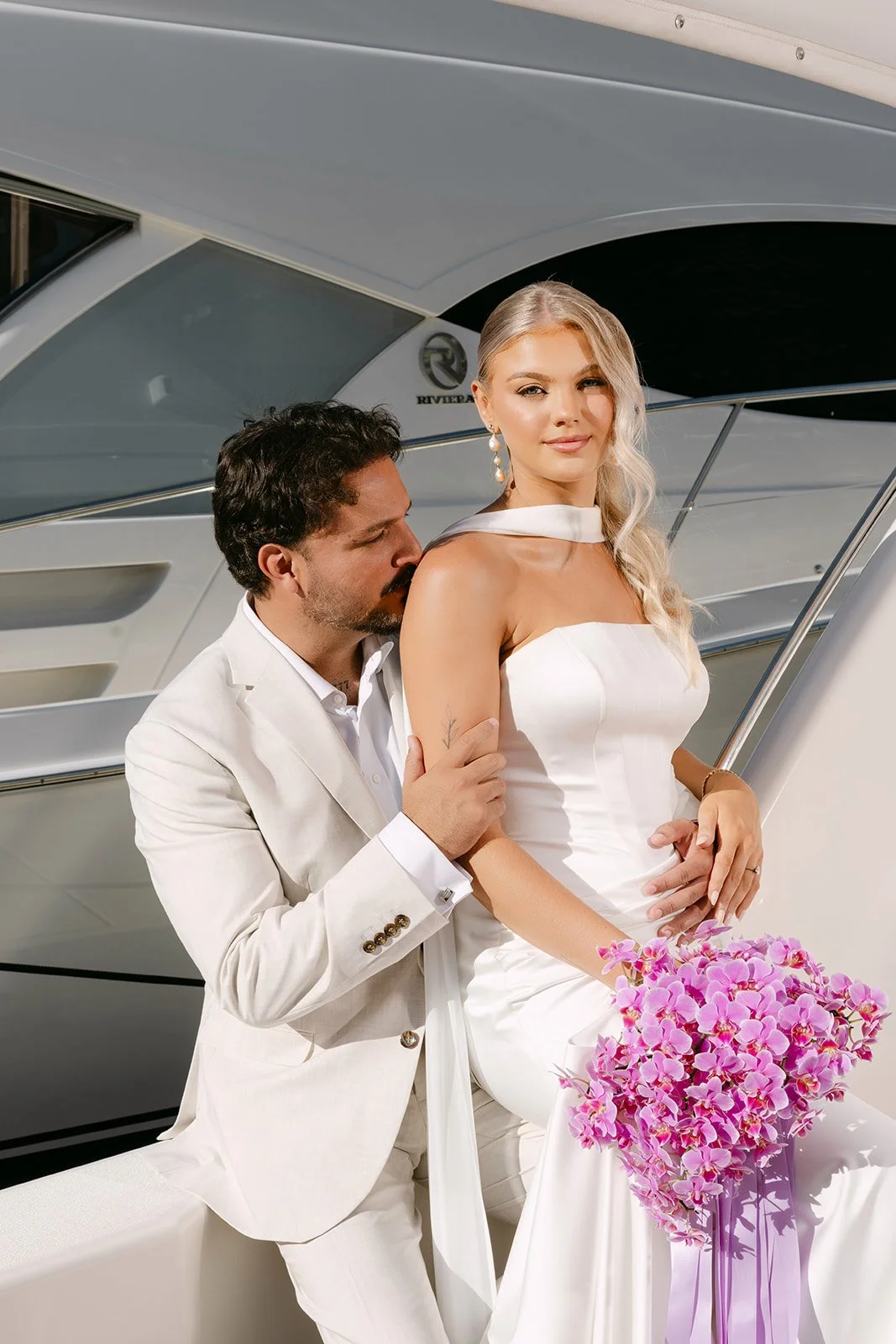 Bride wearing Jane Hill wedding dress with chiffon scarf beside groom on yacht surrounded by pink florals