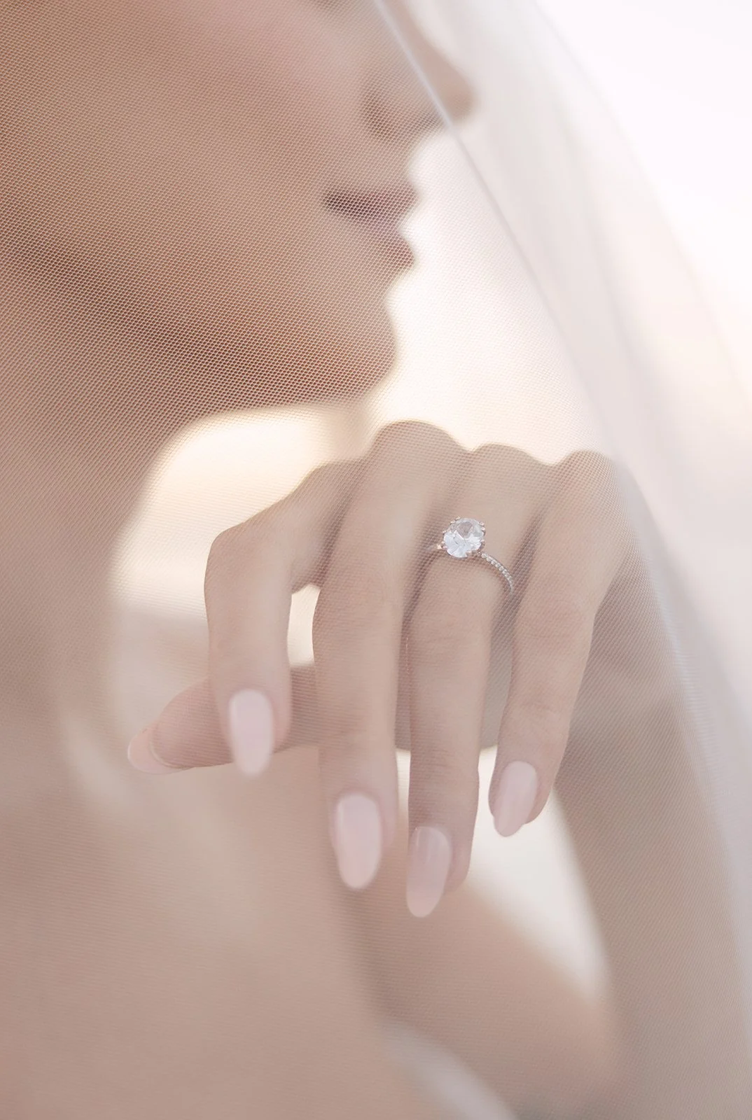 Close-up of bridal nails and engagement ring beneath soft wedding veil