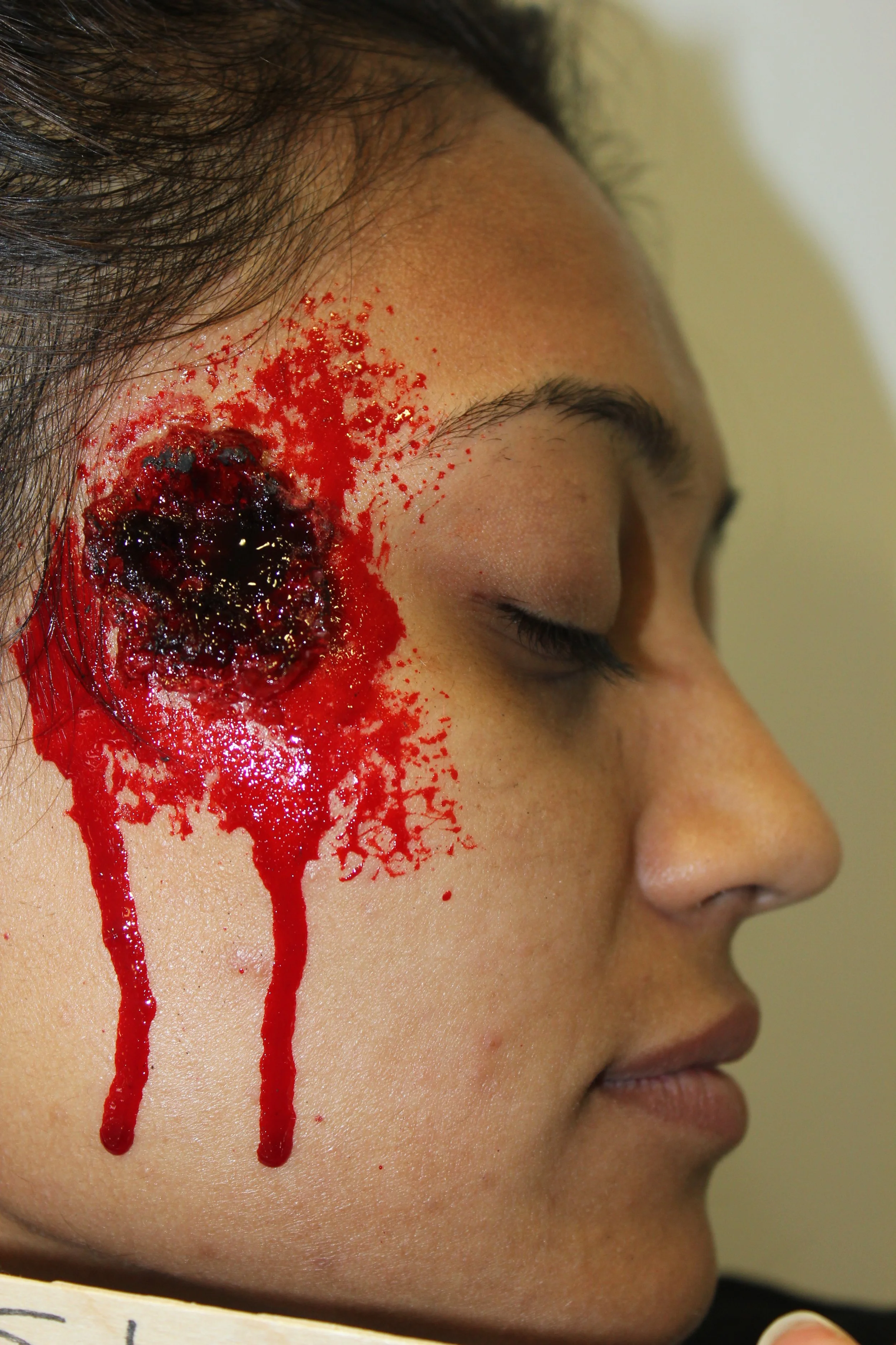 The photo features a realistic bullet wound created with exceptional special effects makeup by Suhaila. The detailed craftsmanship highlights the intensity and authenticity of the exit wound.