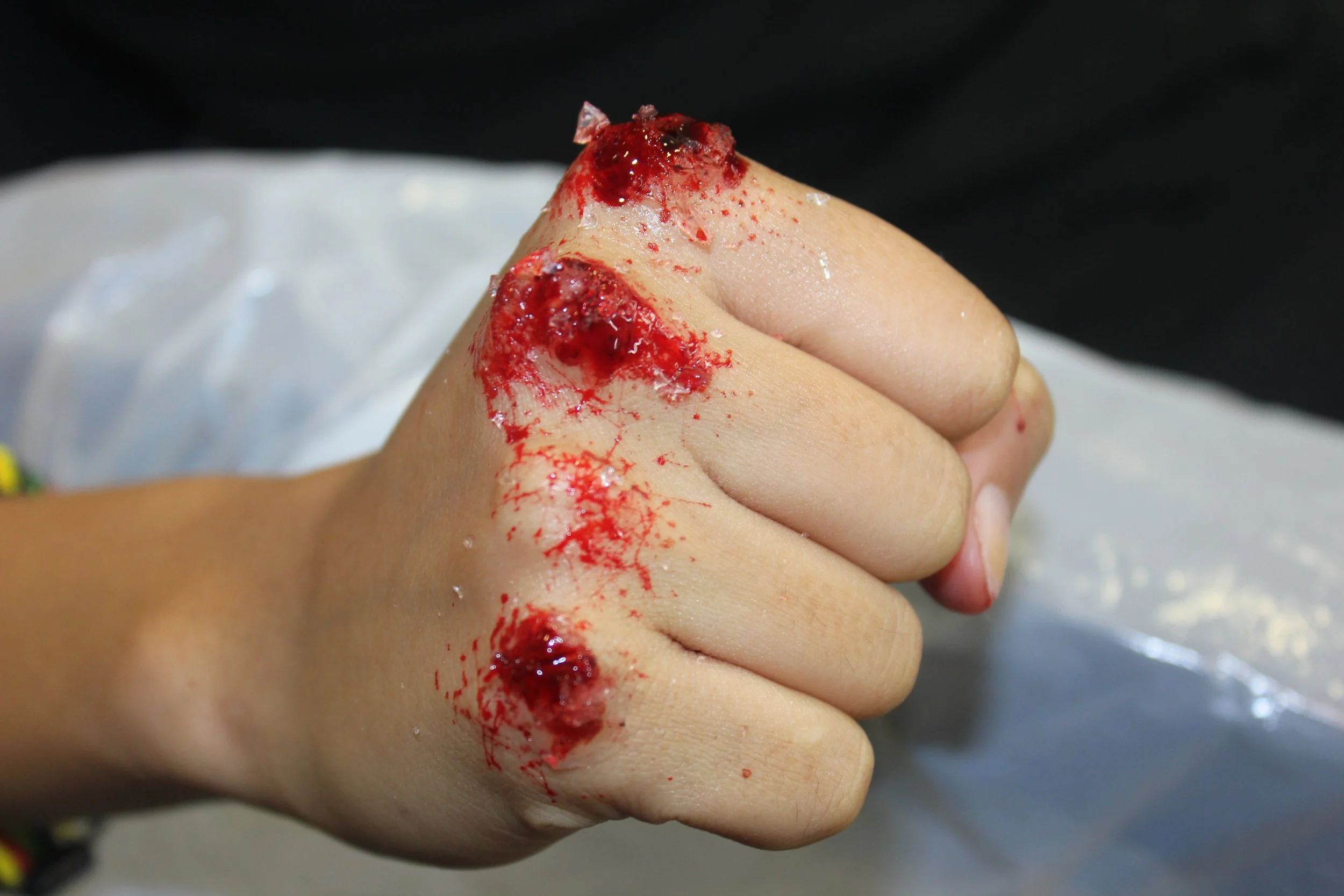 The photo showcases a dramatic scene with shattered glass and a stylized knuckle, enhanced by Suhaila’s striking special effects makeup. The composition captures the raw intensity and intricate detail of the broken glass and bold makeup.