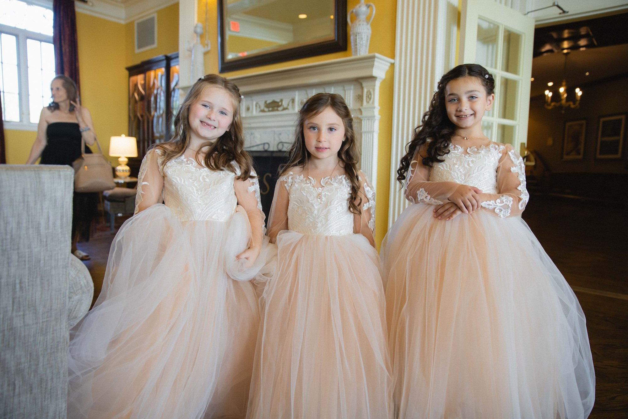 Flower girls in dresses pose for photo in front of fireplace in lobby of The Sagamore Resort