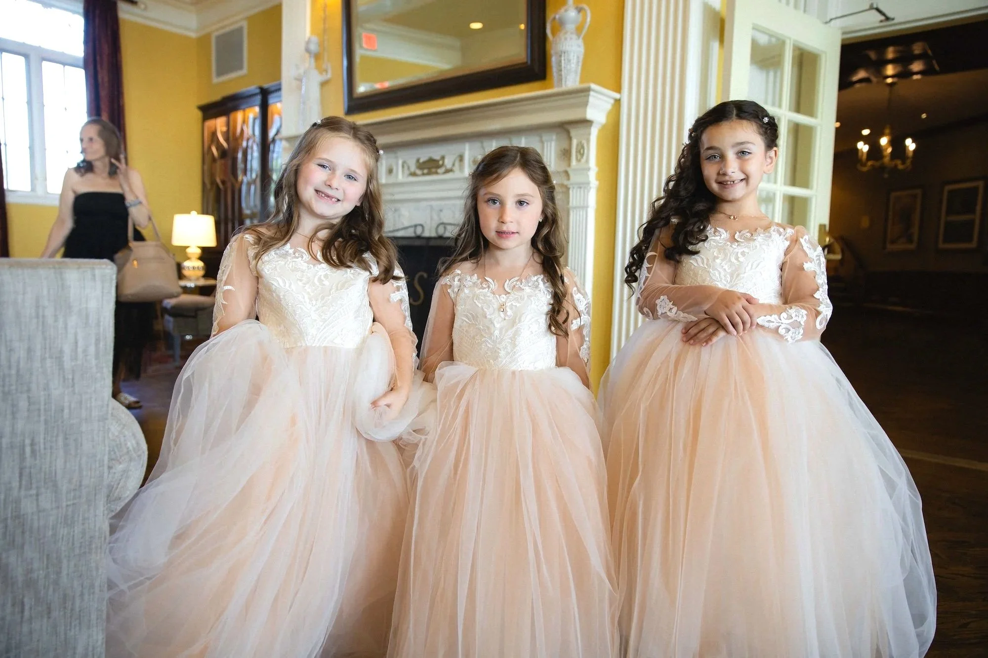 Flower girls in dresses pose for photo in front of fireplace in lobby of The Sagamore Resort