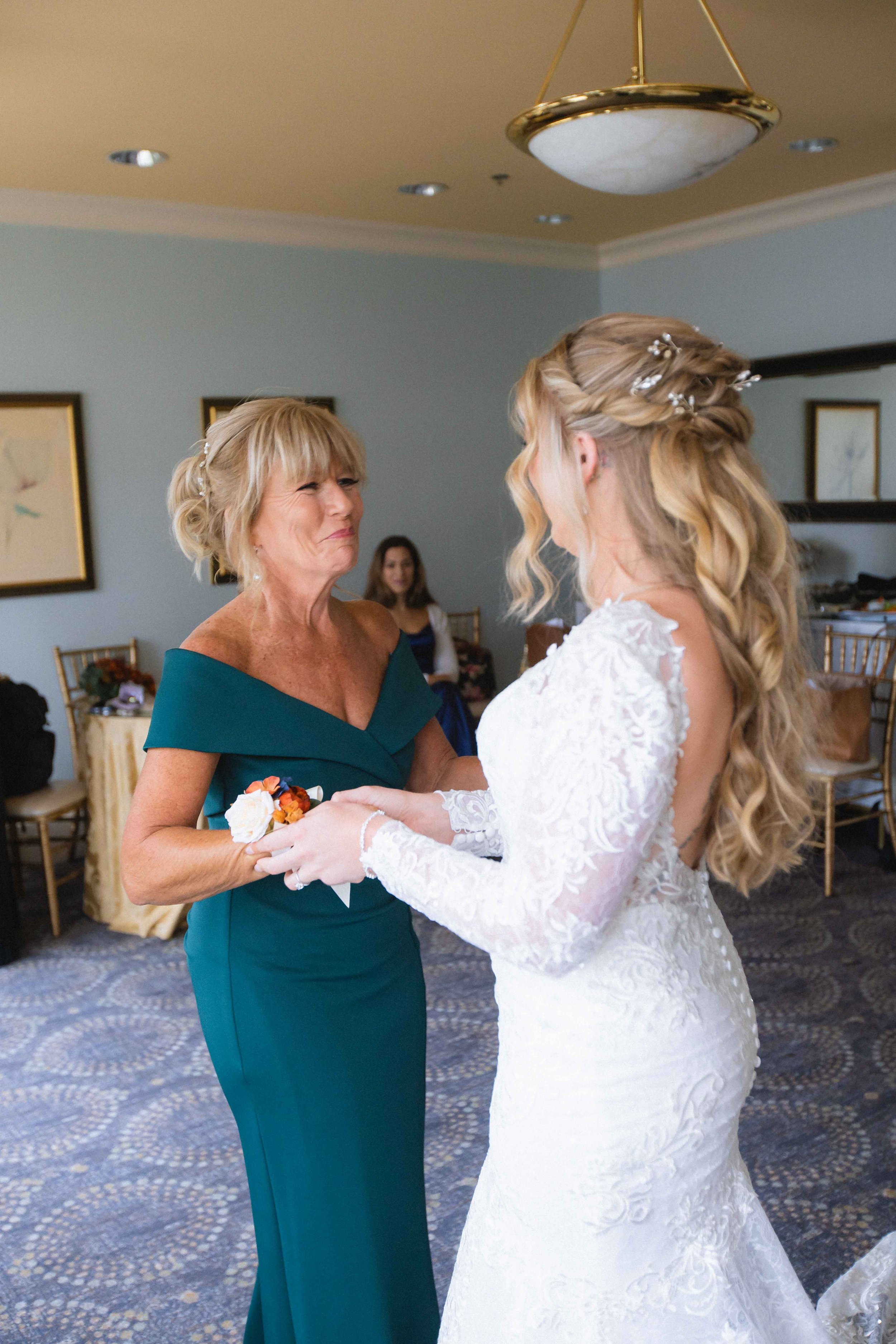 Bride helping mother put corsage on her wrist before ceremony inside the bridal suite at the waterview wedding venue in monroe ct