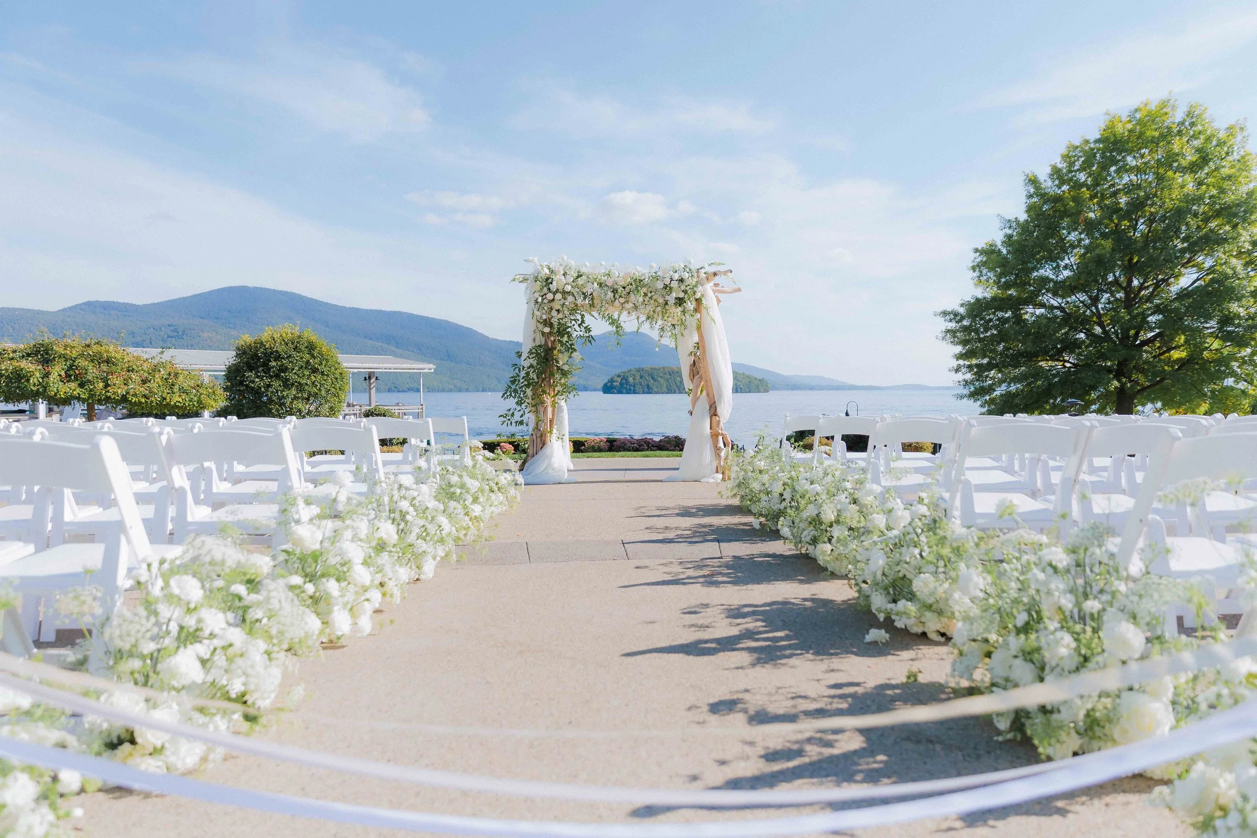beautiful white flowers by Renaissance Floral Design in floral arrangement along aisle and on chuppah before lakeside wedding ceremony at The Sagamore Resort on Lake George in Bolton Landing NY