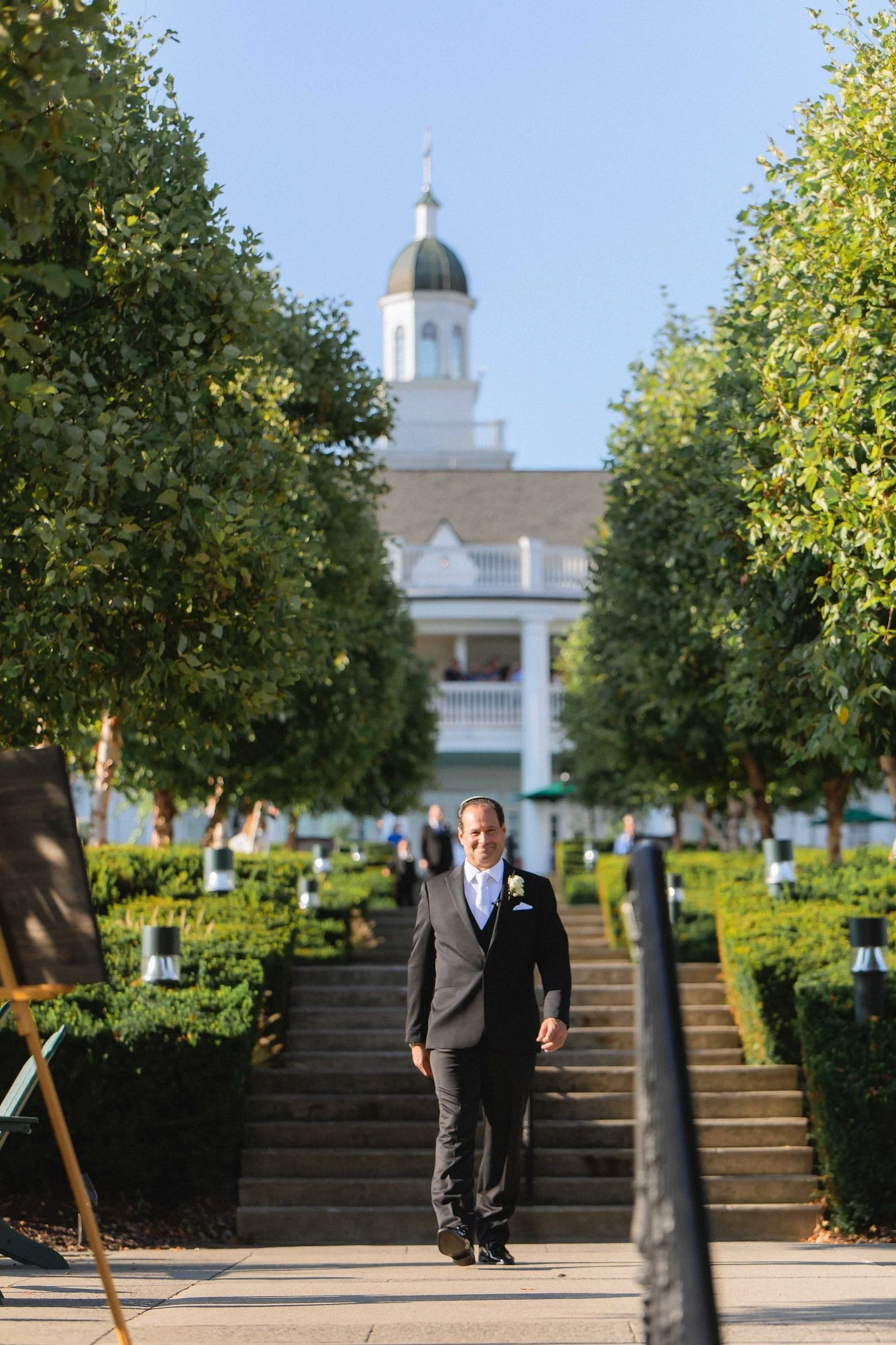 groom walking towards ceremony during processional on steps on back lawn of the sagamore resort in bolton landing on Lake George NY