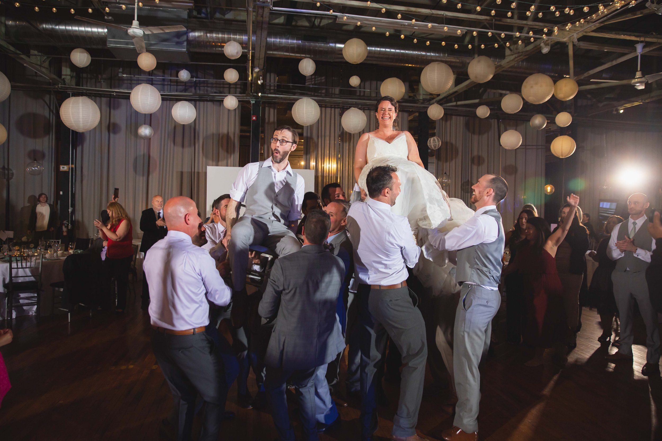 bride and groom smiling and laughing during hora dance chair lift after reception dinner at Saugerties Performing Arts Factory chic industrial wedding venue in upstate NY
