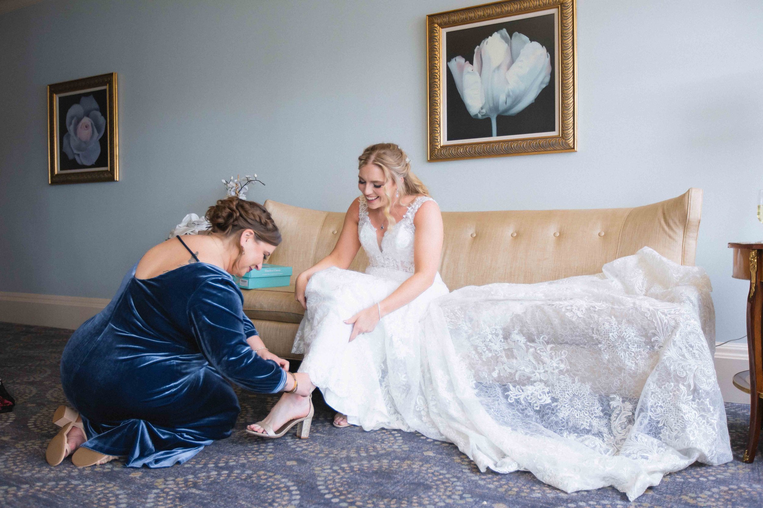 maid of honor helping bride put on her shoes inside the bridal suite at the waterview wedding venue in monroe ct