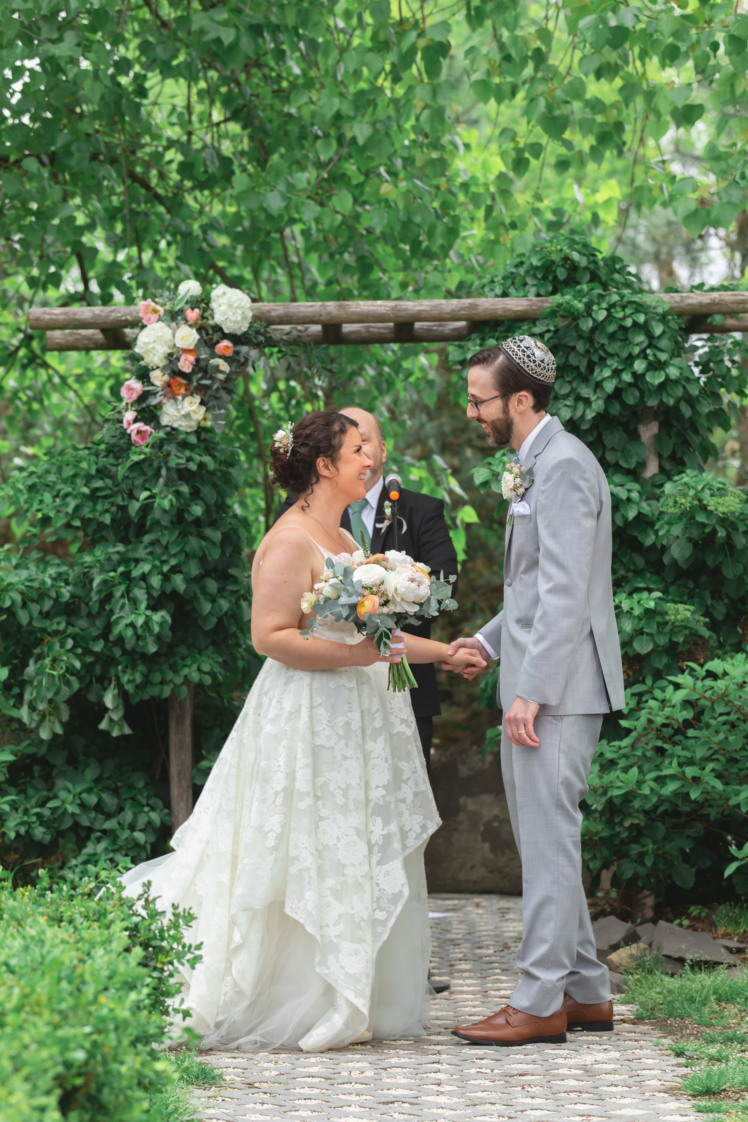 bride and groom just married under floral decorated arbor in verdant summer garden at Saugerties Performing Arts Factory chic industrial wedding venue in upstate NY