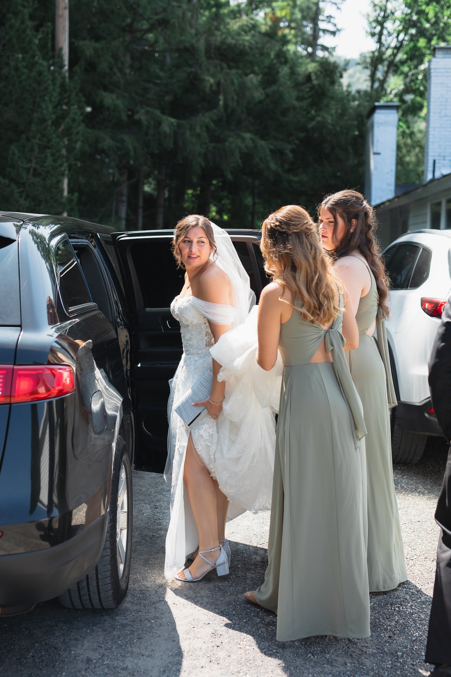 bride in wedding dress helped by bridesmaids getting into limo before ceremony
