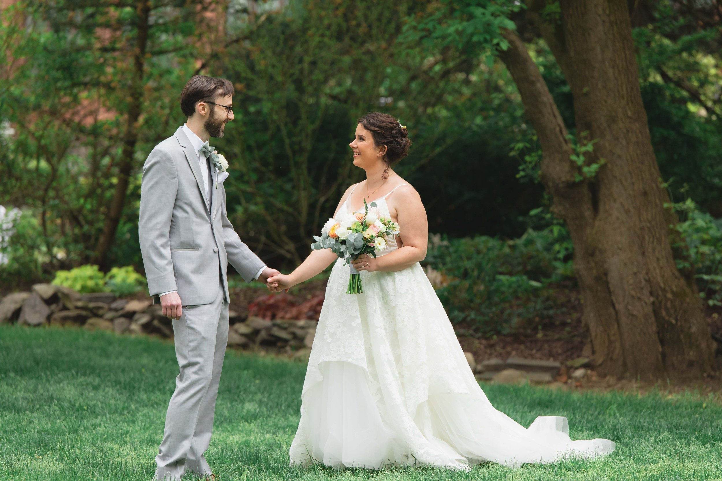 Bride and groom smiling and holding hands during first look in garden in summer at Saugerties Performing Arts Factory wedding venue in upstate NY