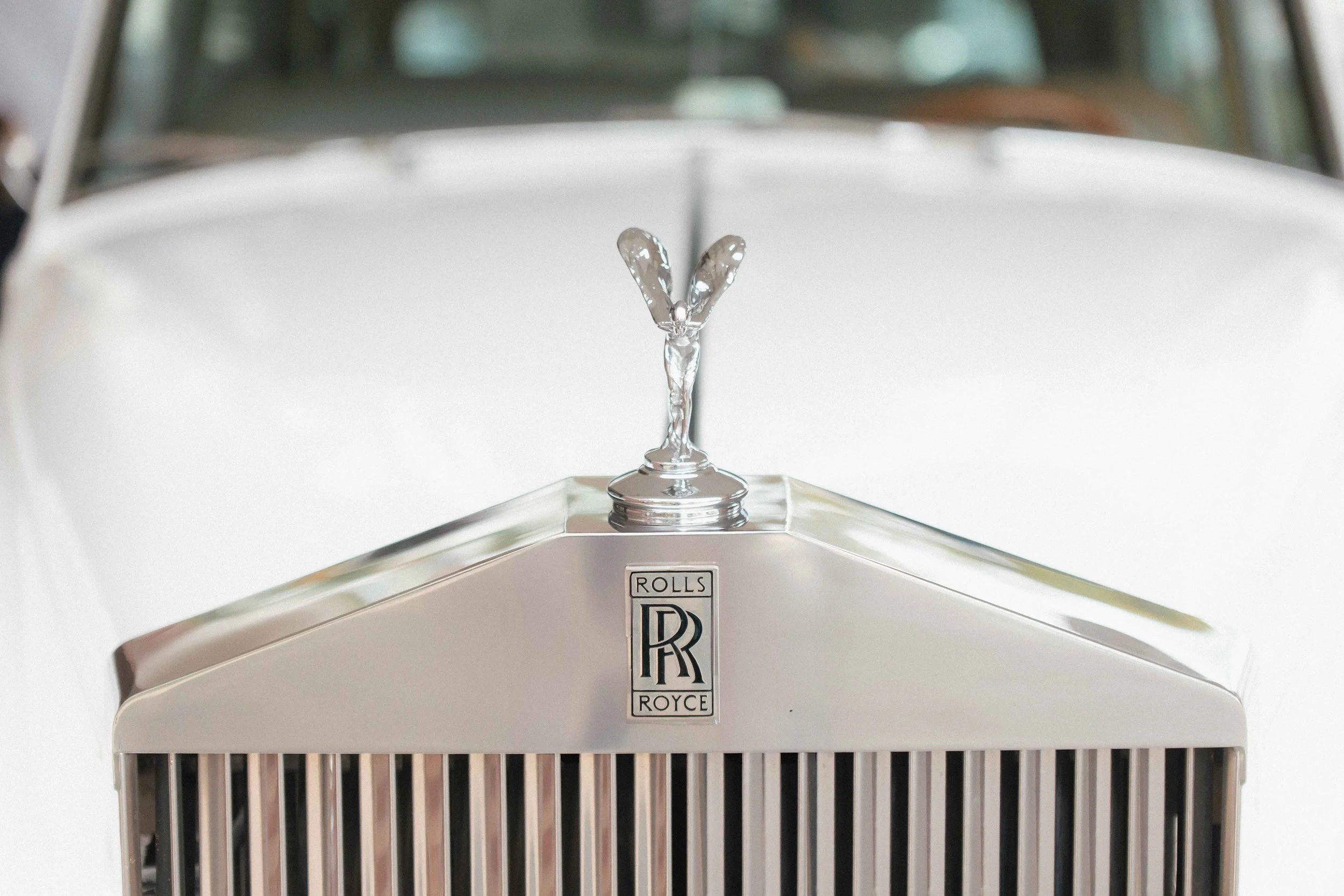 Close-up of a vintage Rolls-Royce car hood ornament featuring the Spirit of Ecstasy mascot mounted on the front grille.