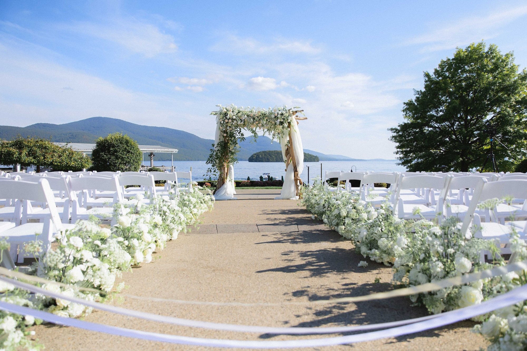 Aisle of wedding ceremony decorated with flowers leading to chuppah decorated with beautiful florals lakeside overlooking mountains at the sagamore resort in Bolton Landing on Lake George NY