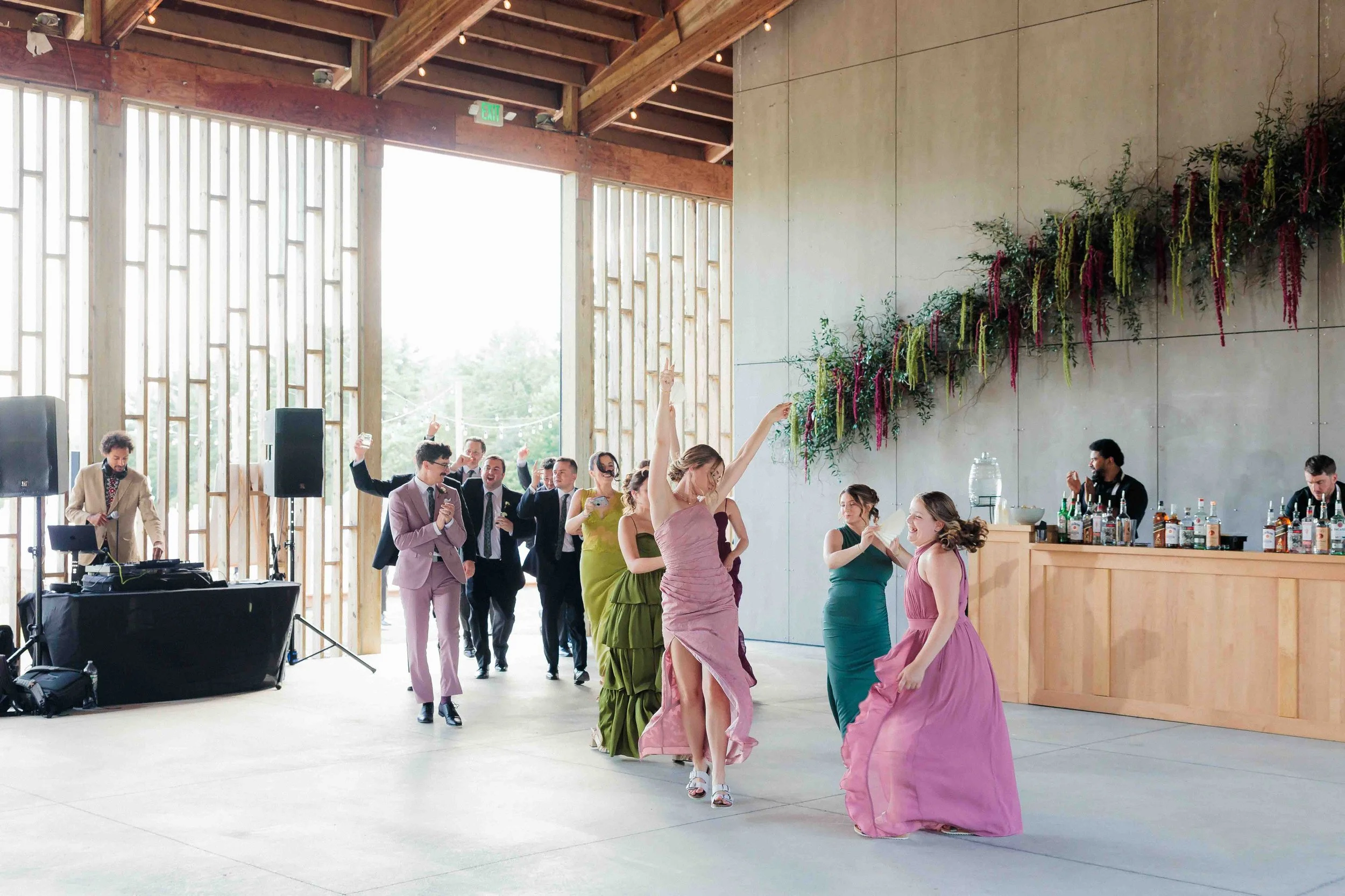 Group of people dancing and celebrating indoors at a wedding reception, with some individuals raising their hands and smiling.
