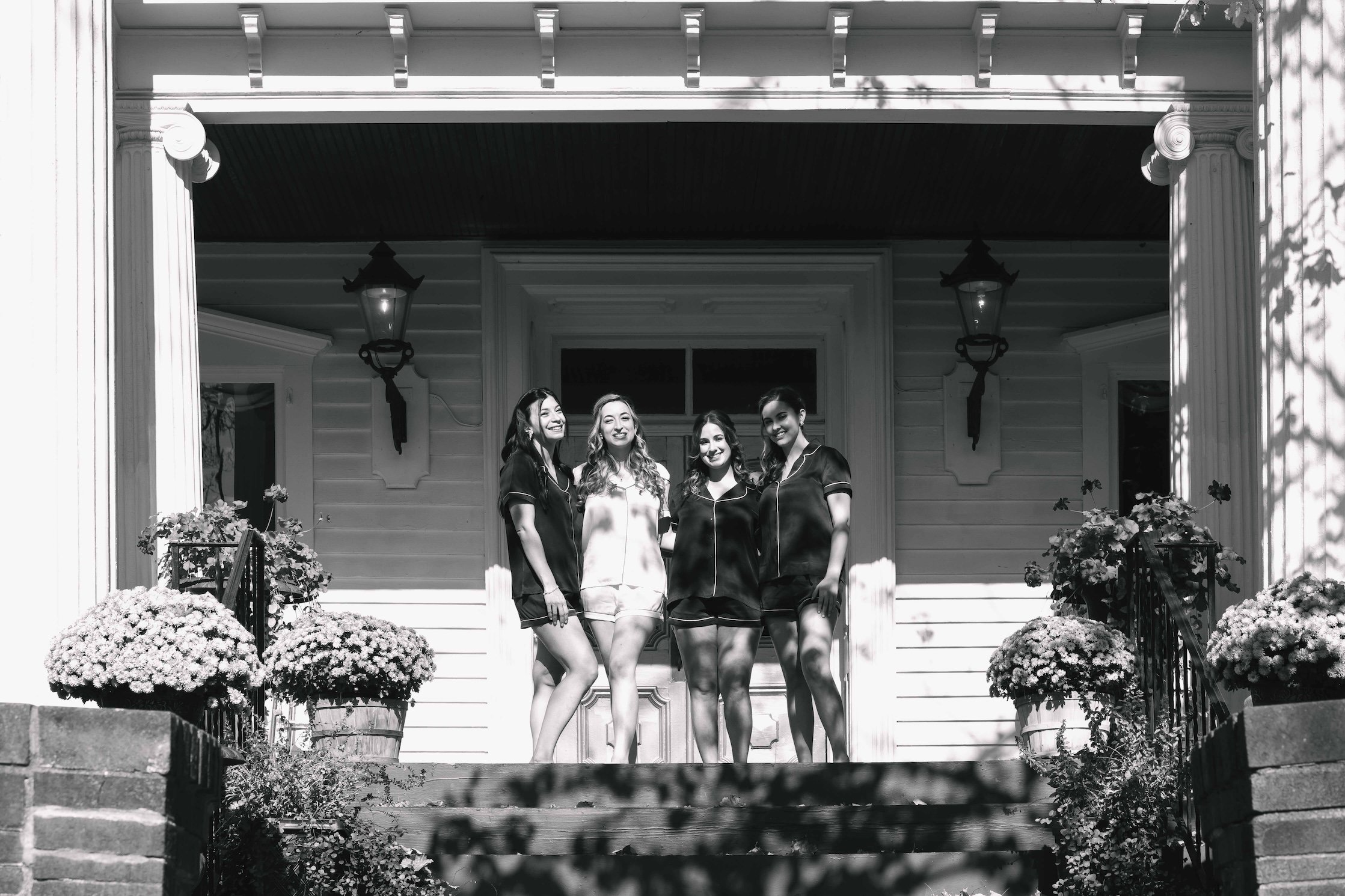 bride and bridesmaids laughing and smiling outside on regal front porch of historic home in upstate NY fall wedding at FEAST at Round Hill wedding venue in Washingtonville NY