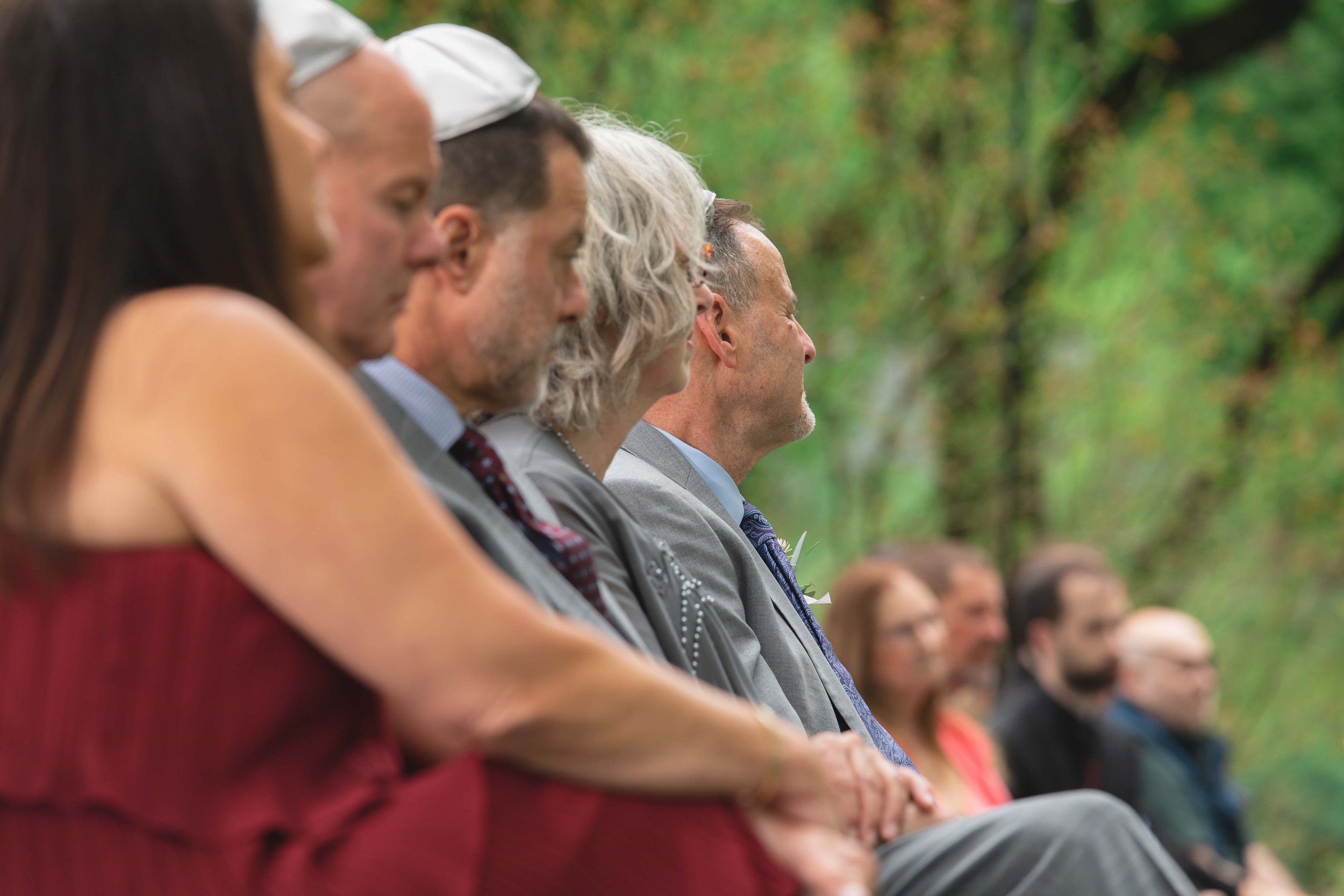 parents of groom during wedding ceremony in verdant summer garden at Saugerties Performing Arts Factory chic industrial wedding venue in upstate NY