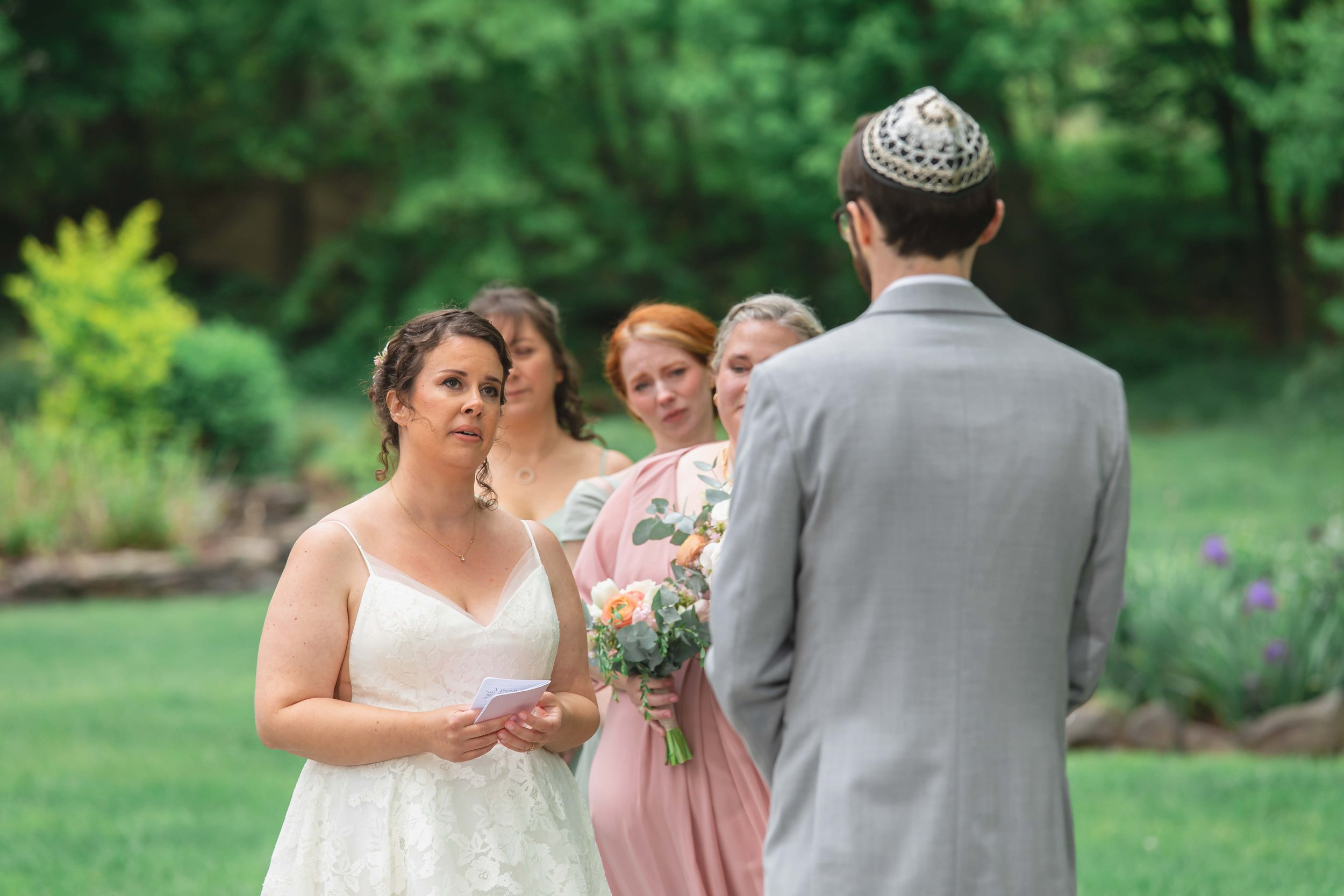 bride reading vows to groom in verdant summer garden at Saugerties Performing Arts Factory chic industrial wedding venue in upstate NY