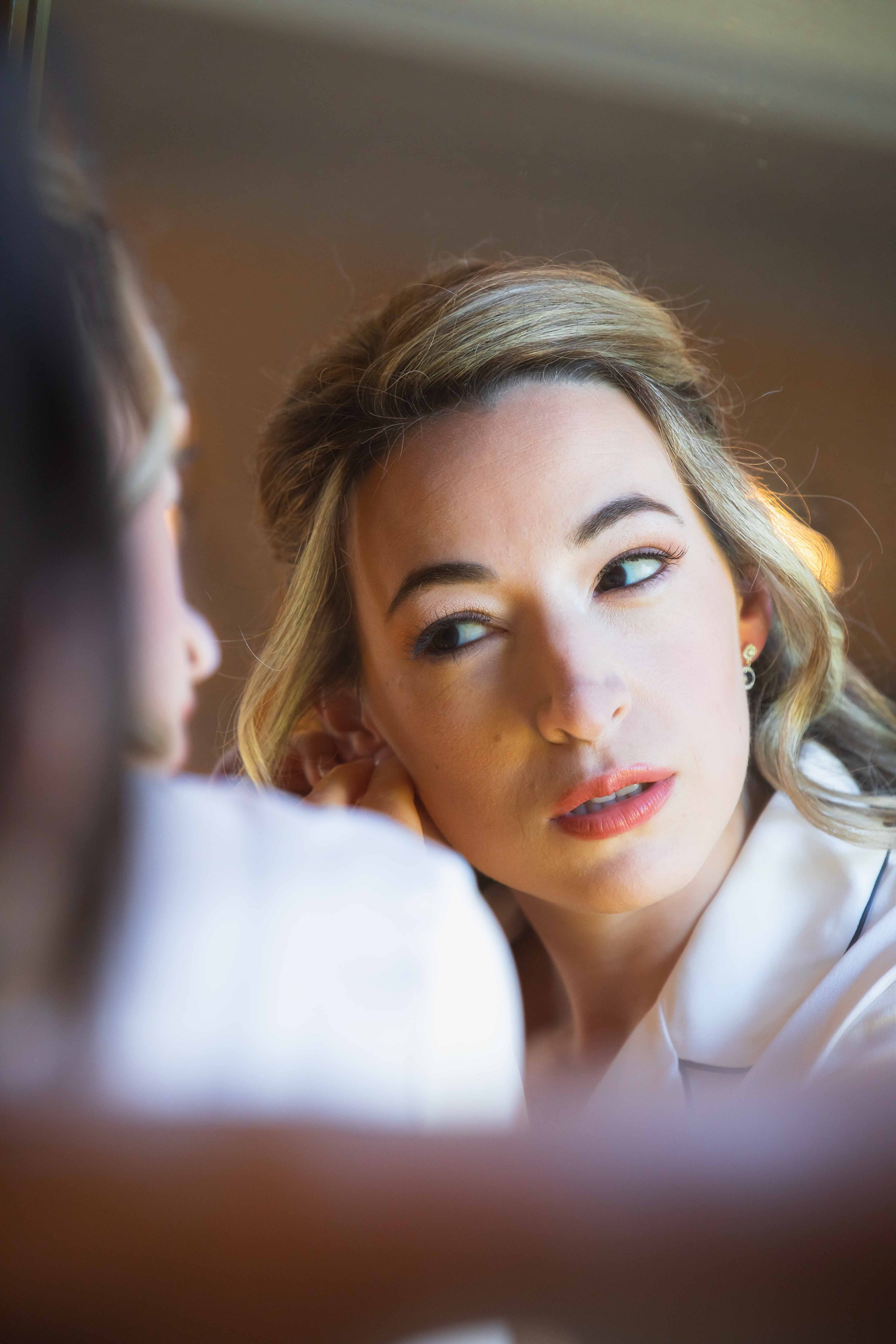 bride puts on sapphire and diamond earrings in natural window light in historic home in upstate NY fall wedding at FEAST at Round Hill wedding venue in Washingtonville NY