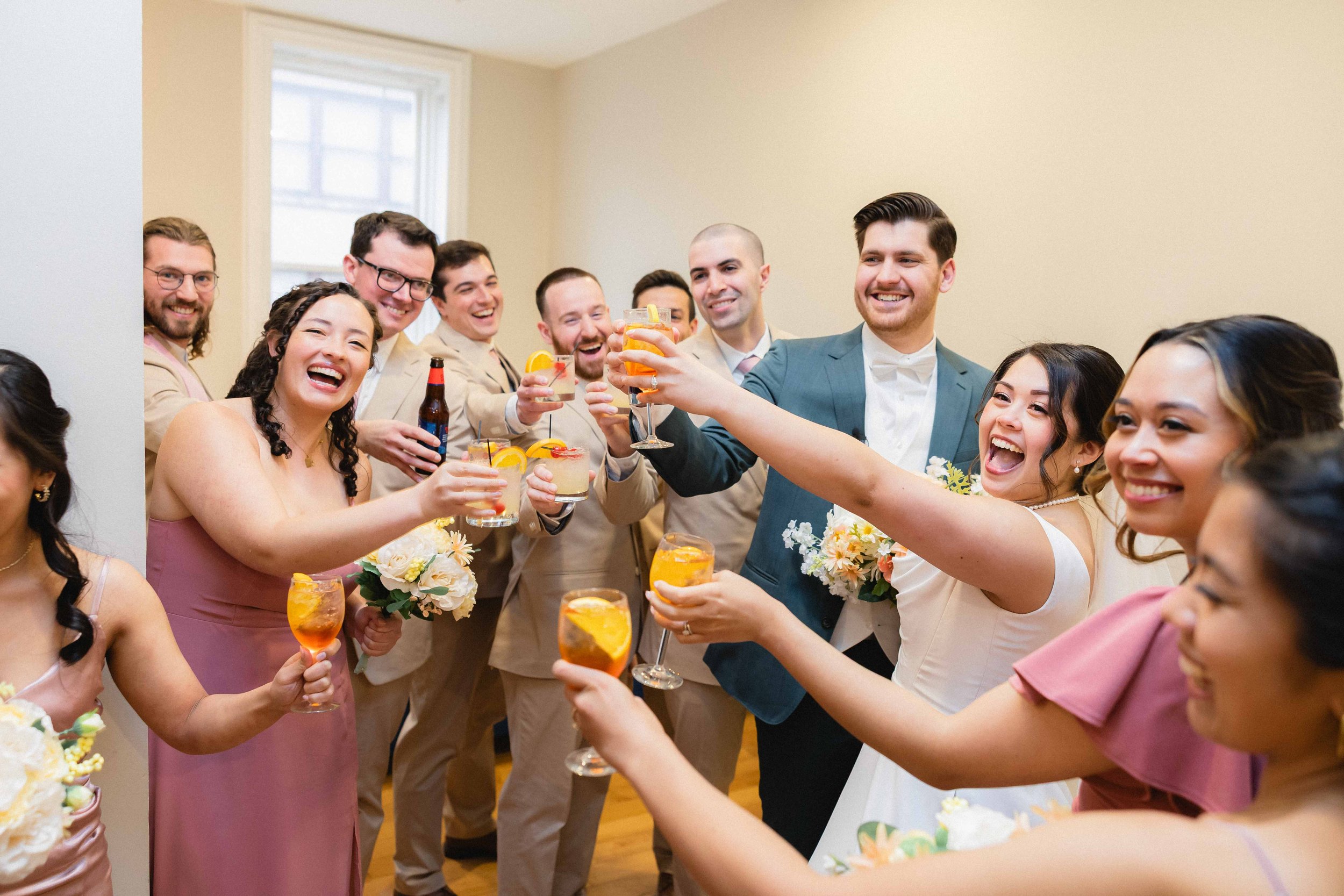 Group of people at a wedding celebration raising glasses in toast, smiling and holding drinks with fruit garnishes.