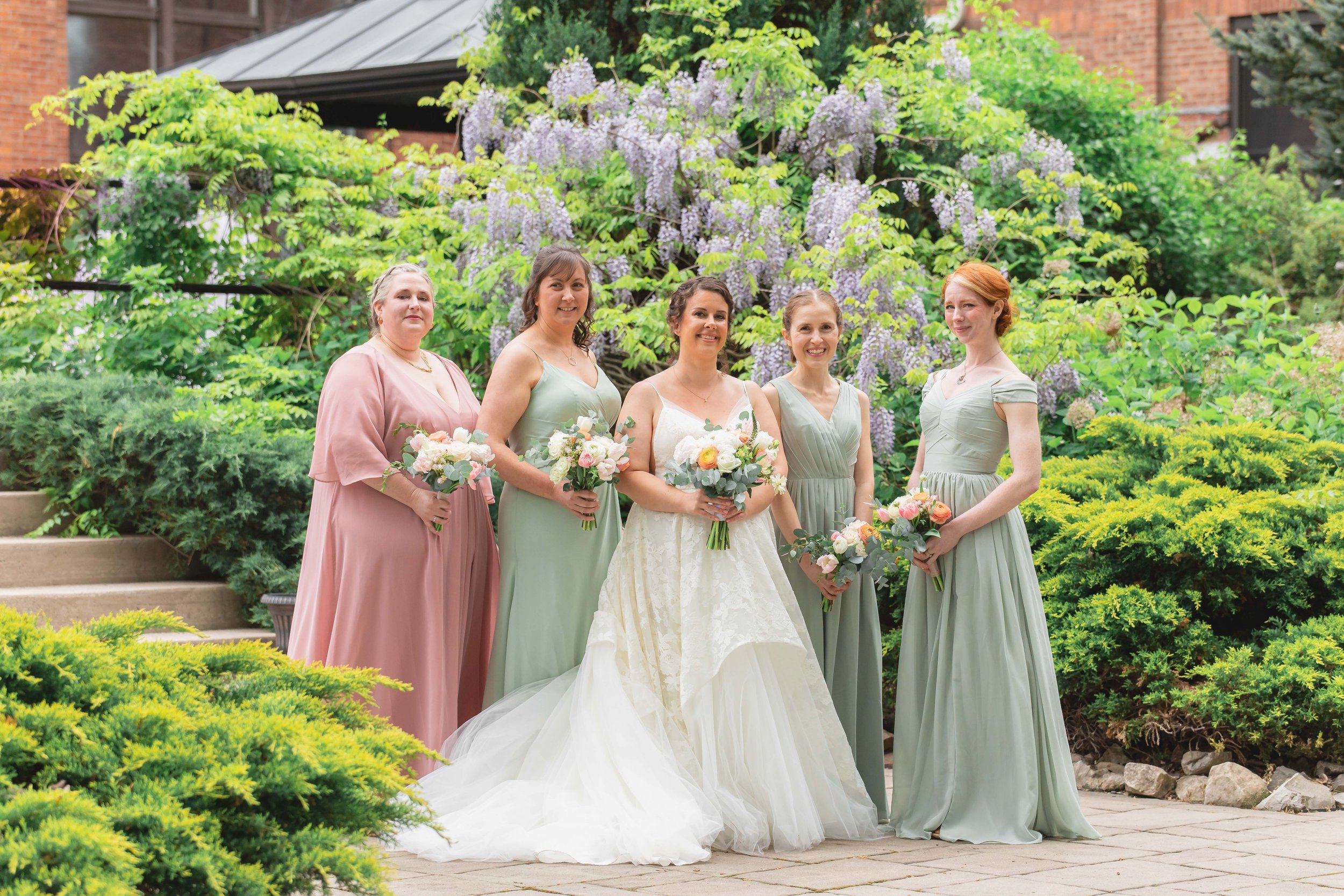 Bride and bridesmaids in verdant summer garden at Saugerties Performing Arts Factory wedding venue in upstate NY