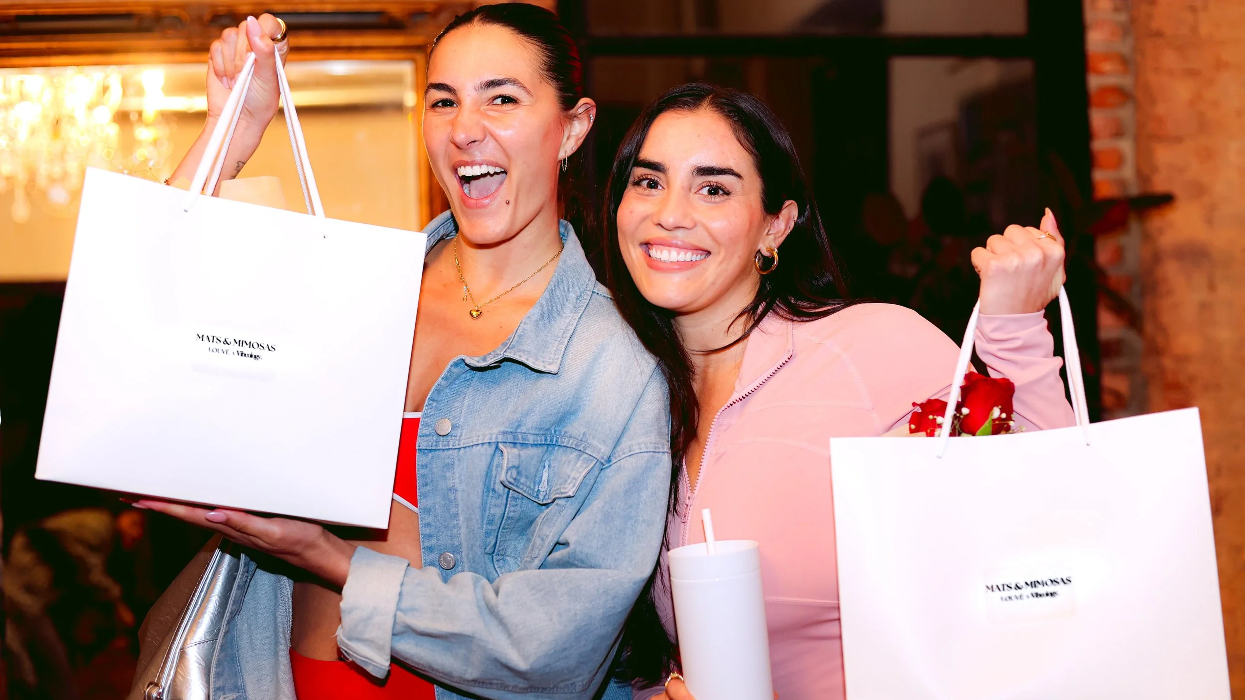 Two women smiling and holding shopping bags at a retail store or shopping mall.
