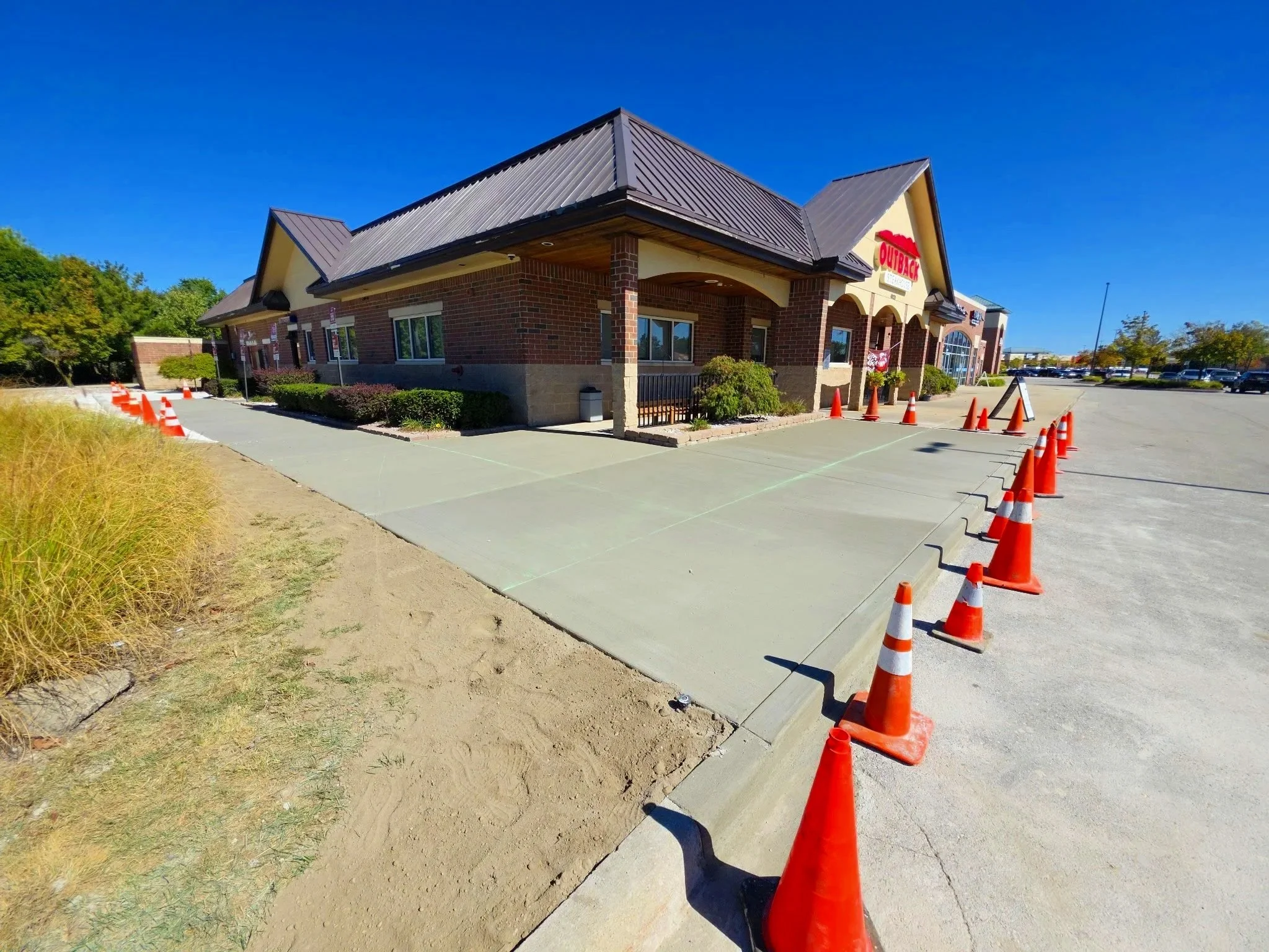 Empty restaurant drive-thru and parking lot with orange traffic cones and some construction areas, under a clear blue sky.