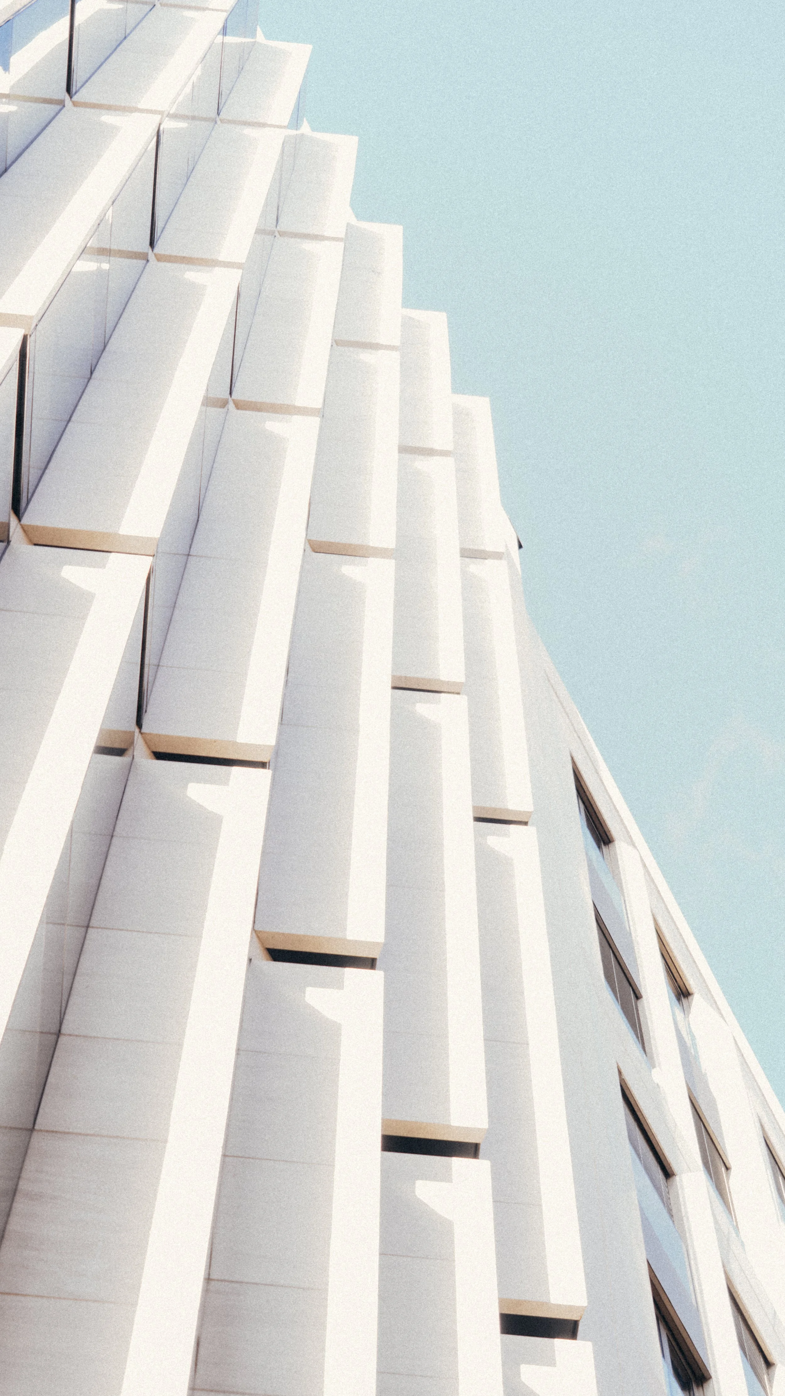 A modern white building with irregularly placed windows and protruding architectural features against a clear blue sky.