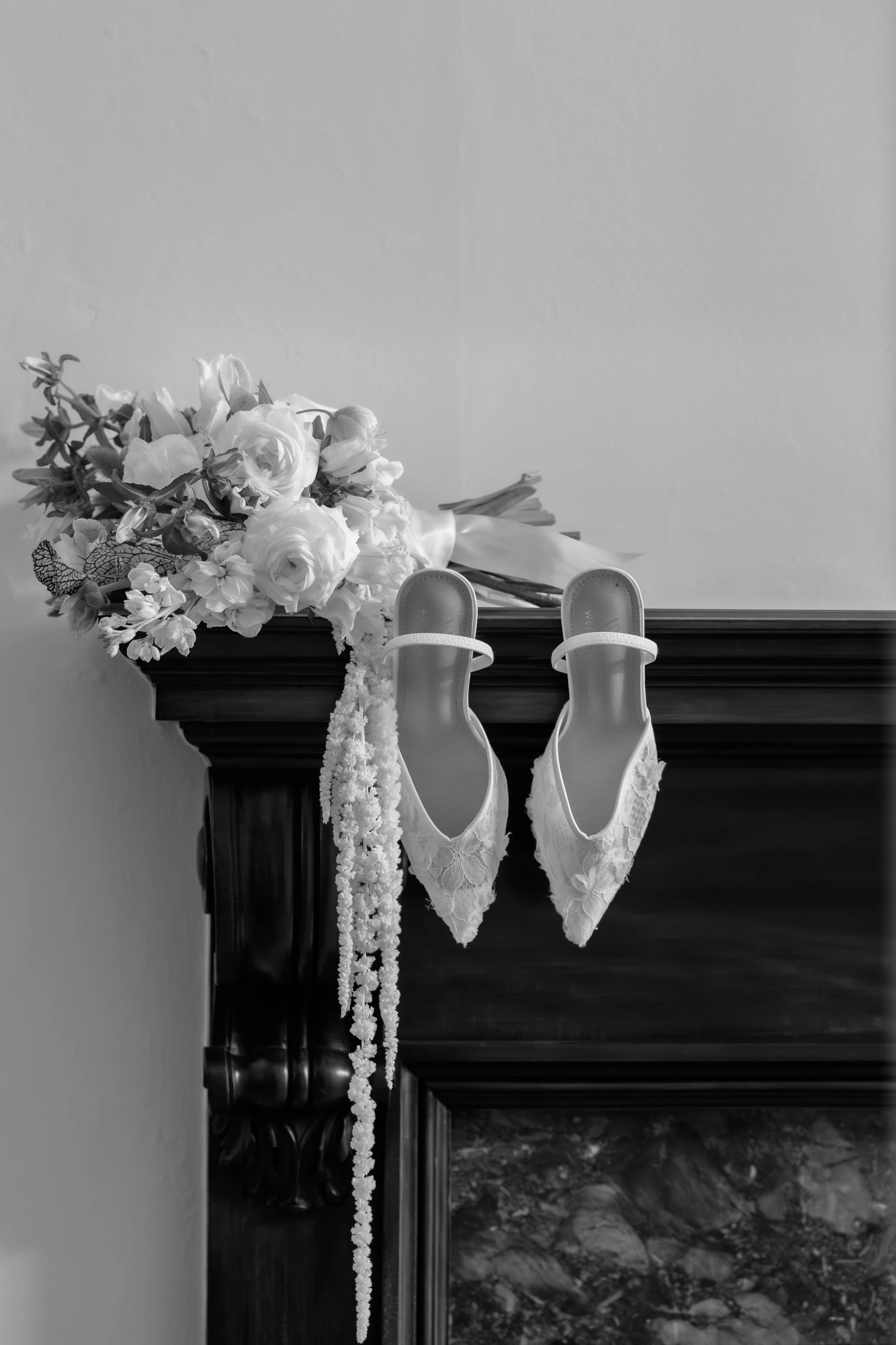Wedding bouquet, lace bridal heels, and floral accessories arranged on a fireplace mantel before the ceremony.