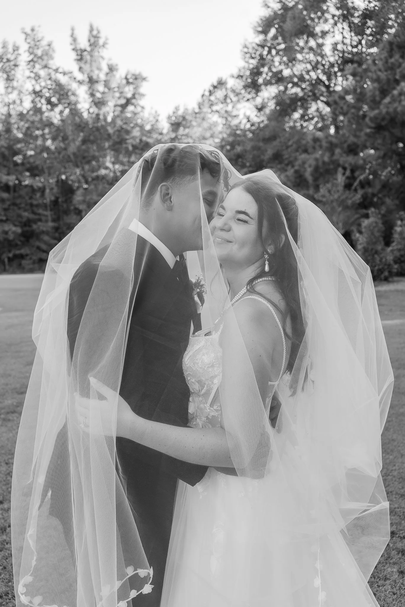Bride and groom embracing beneath a flowing wedding veil during an outdoor North Carolina wedding portrait.