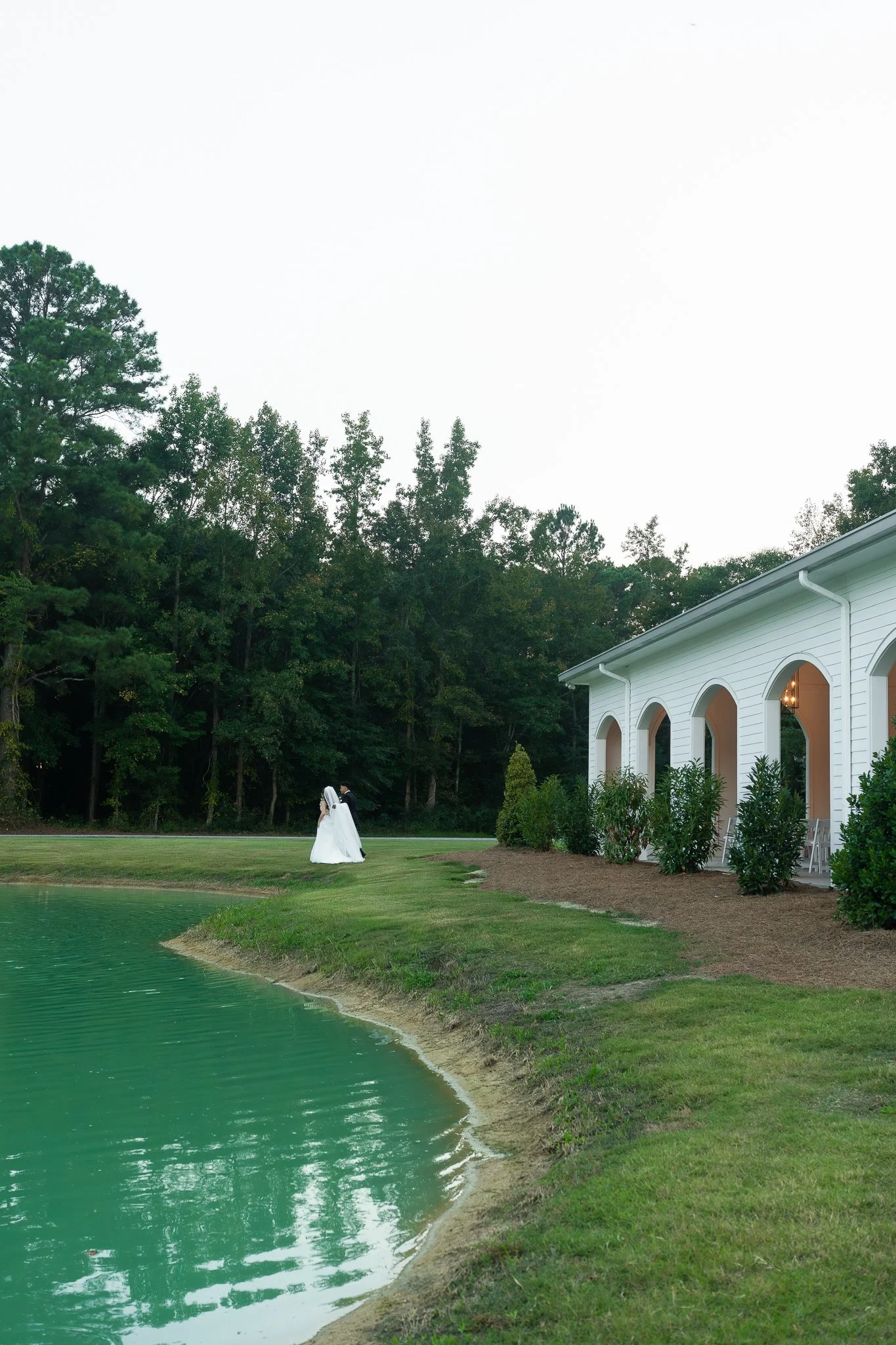 Bride and groom standing beside a scenic pond outside a North Carolina wedding venue during golden hour.