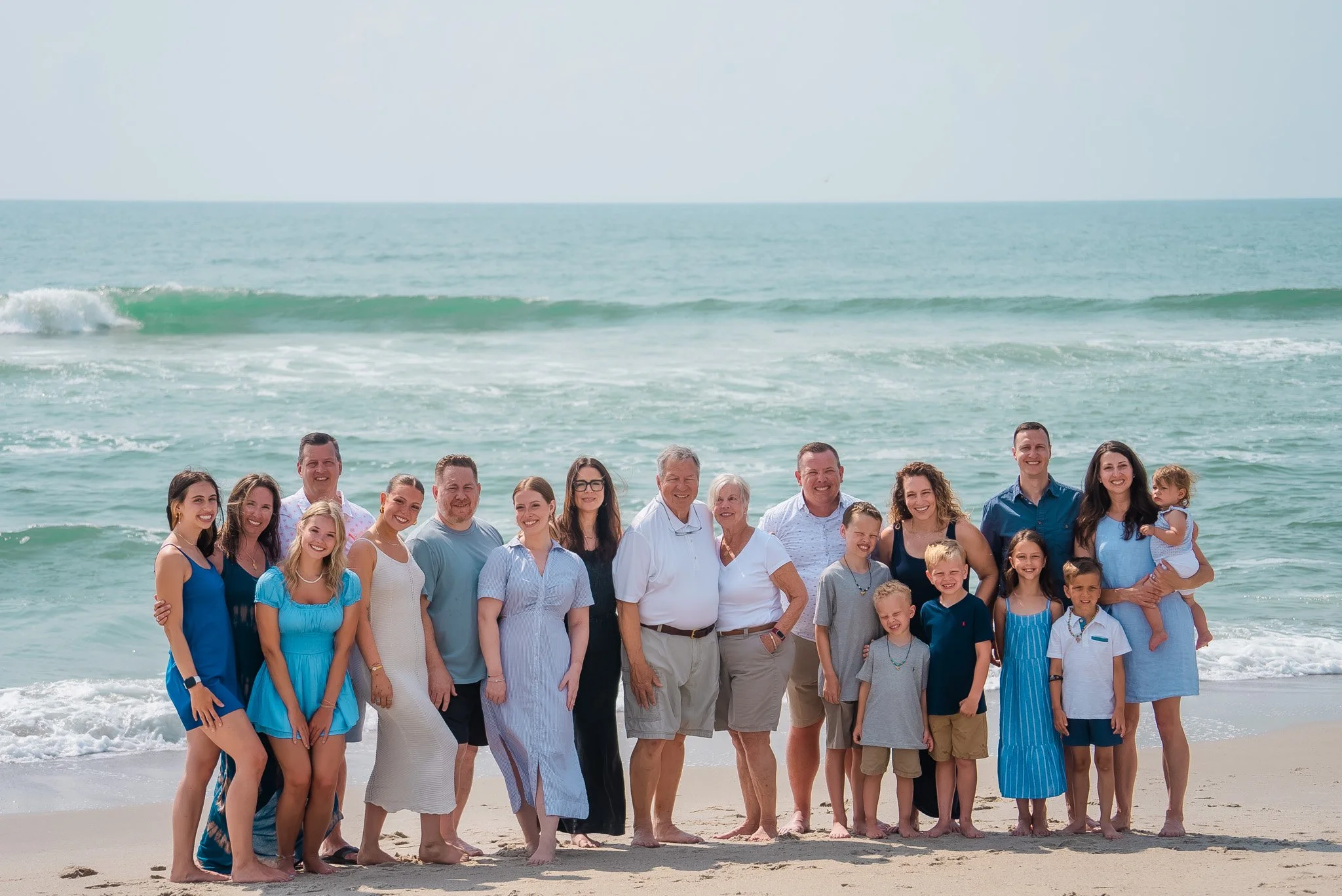 Group of people on a beach posing for a photo, with ocean waves in the background.