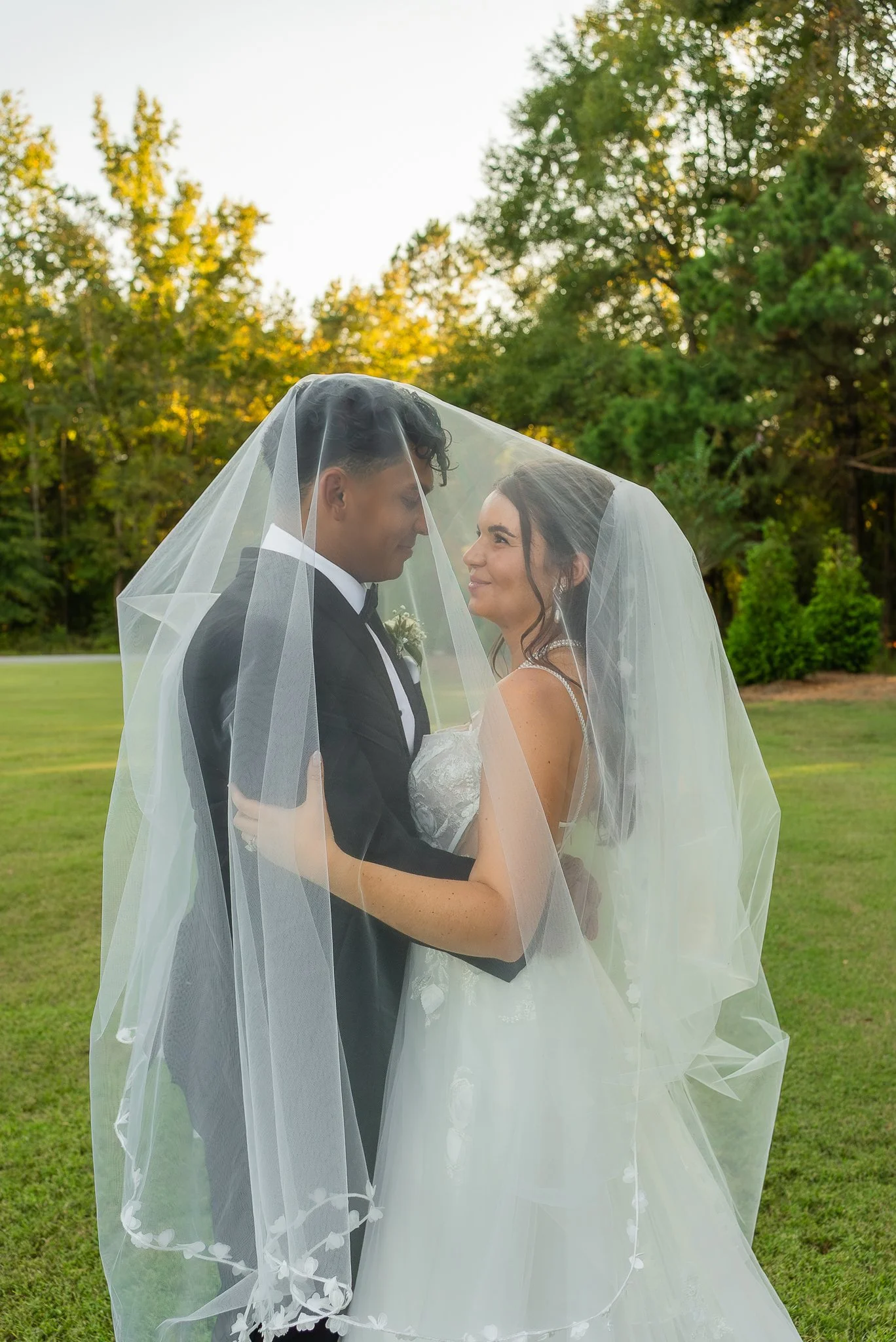 Bride and groom embracing beneath a flowing wedding veil during golden hour wedding portraits.