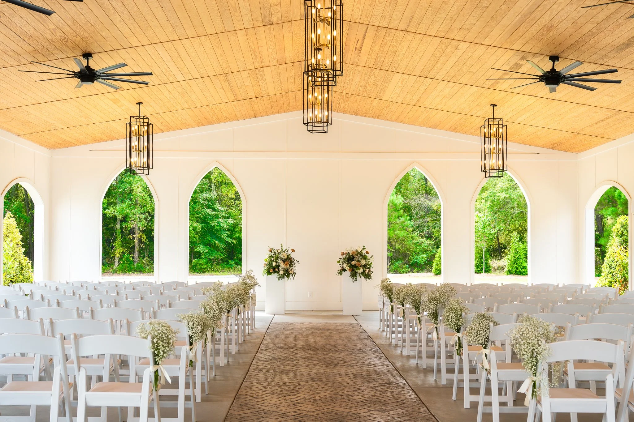 Elegant wedding ceremony venue with white chairs, floral arrangements, and arched windows overlooking lush greenery.