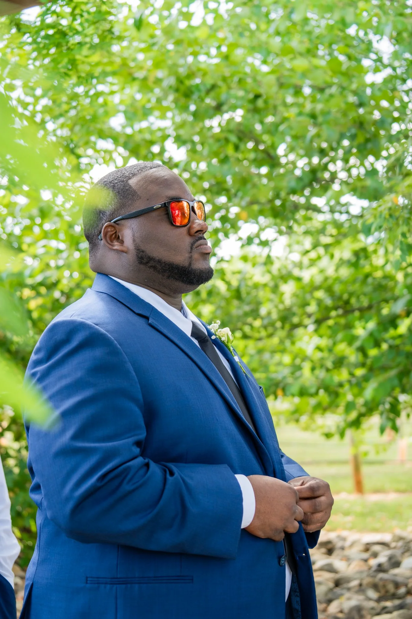 Groom JaNathan in navy suit with sunglasses posing at Spinning Leaf vineyard wedding venue in North Carolina