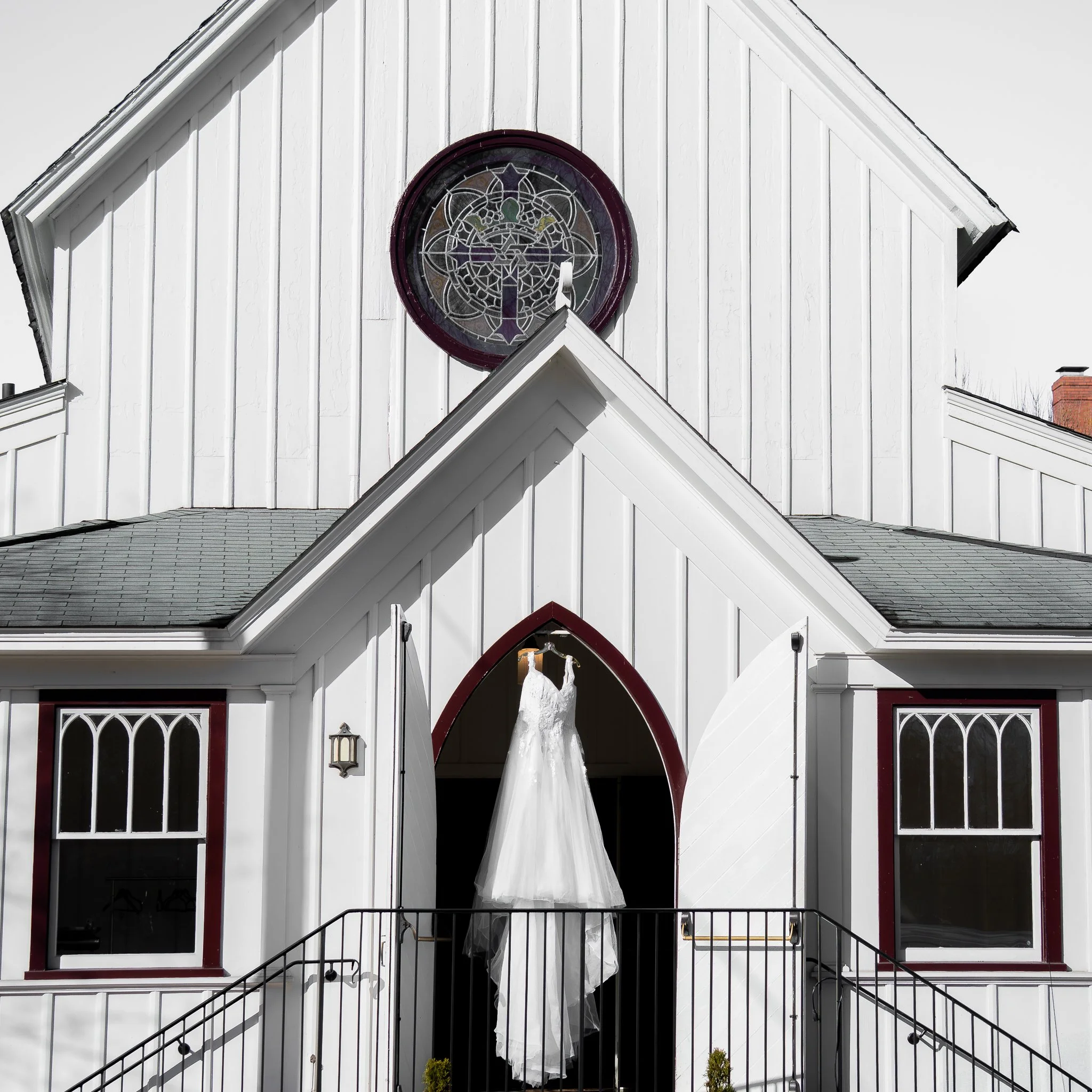 White church with stained glass window and a wedding dress hanging at the entrance.