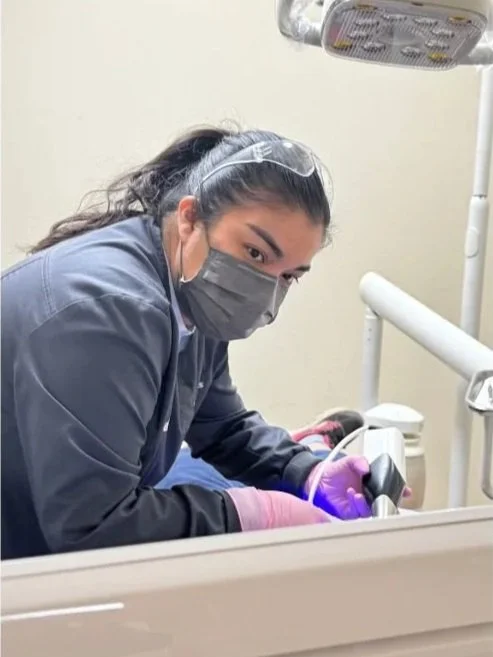 Dental hygienist wearing a mask and gloves, working on a patient in a dental office.