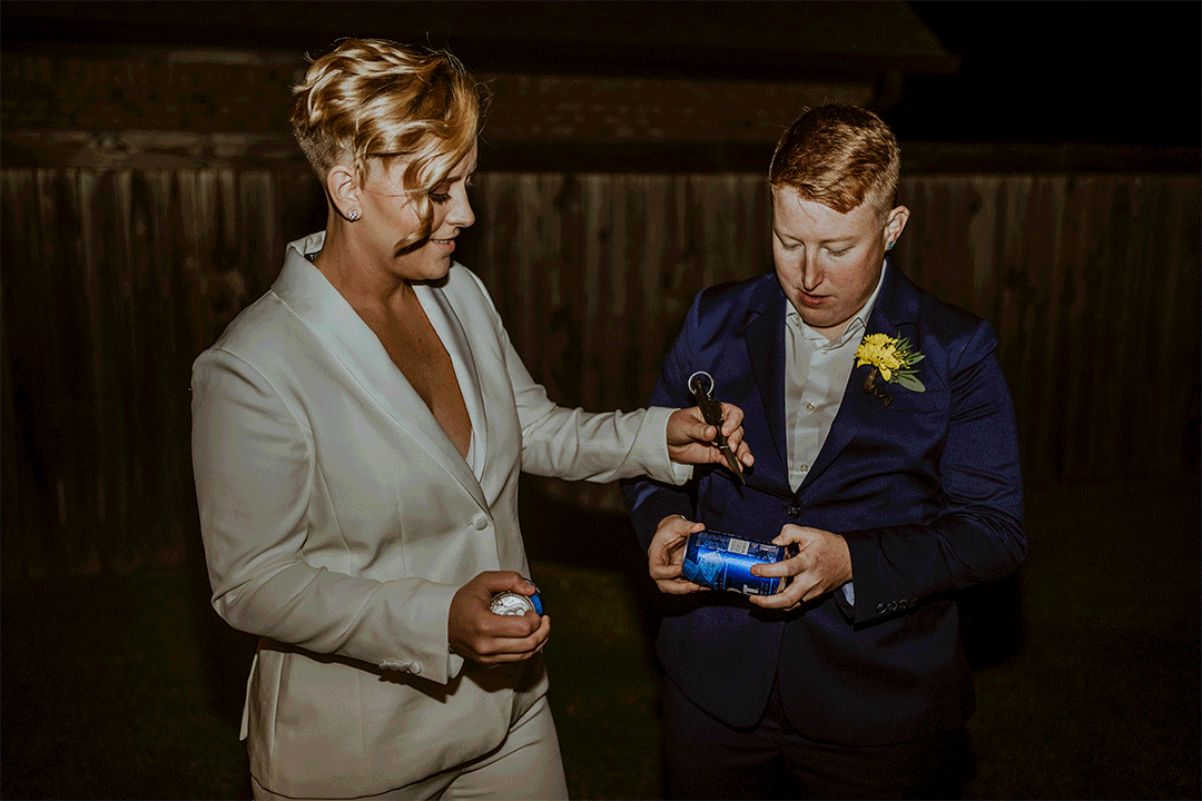 Two people in formal attire, one in a white suit holding a soda can with a tool while the other holds another object, standing outdoors at night.