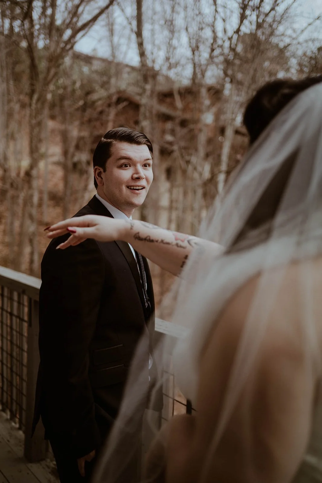 Man in suit smiling at woman in wedding dress with tattoos, outdoor setting.