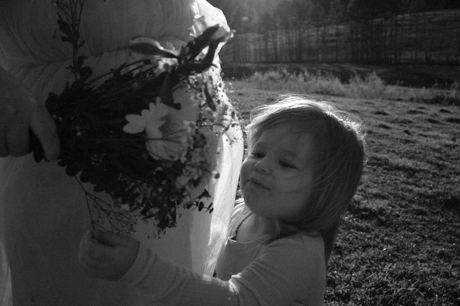 Black and white photo of a child holding a bouquet in a scenic outdoor setting.