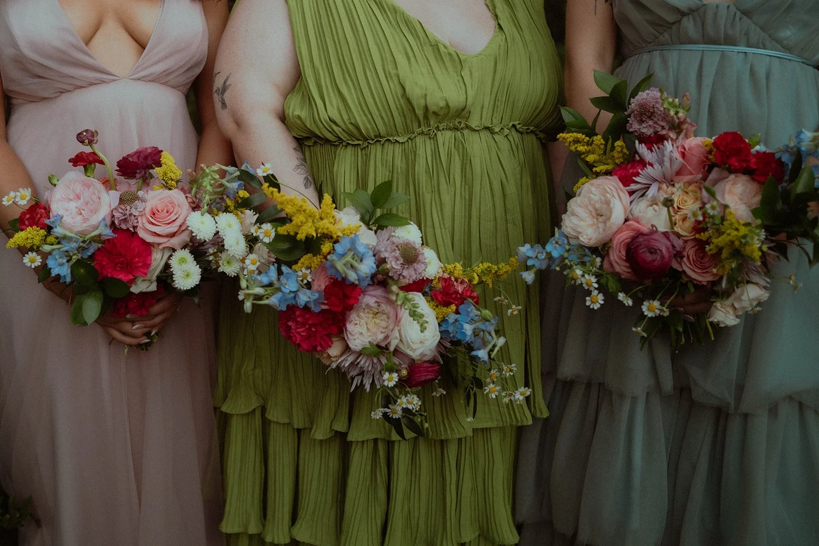 Three people in colorful dresses holding vibrant flower bouquets with various blooms.