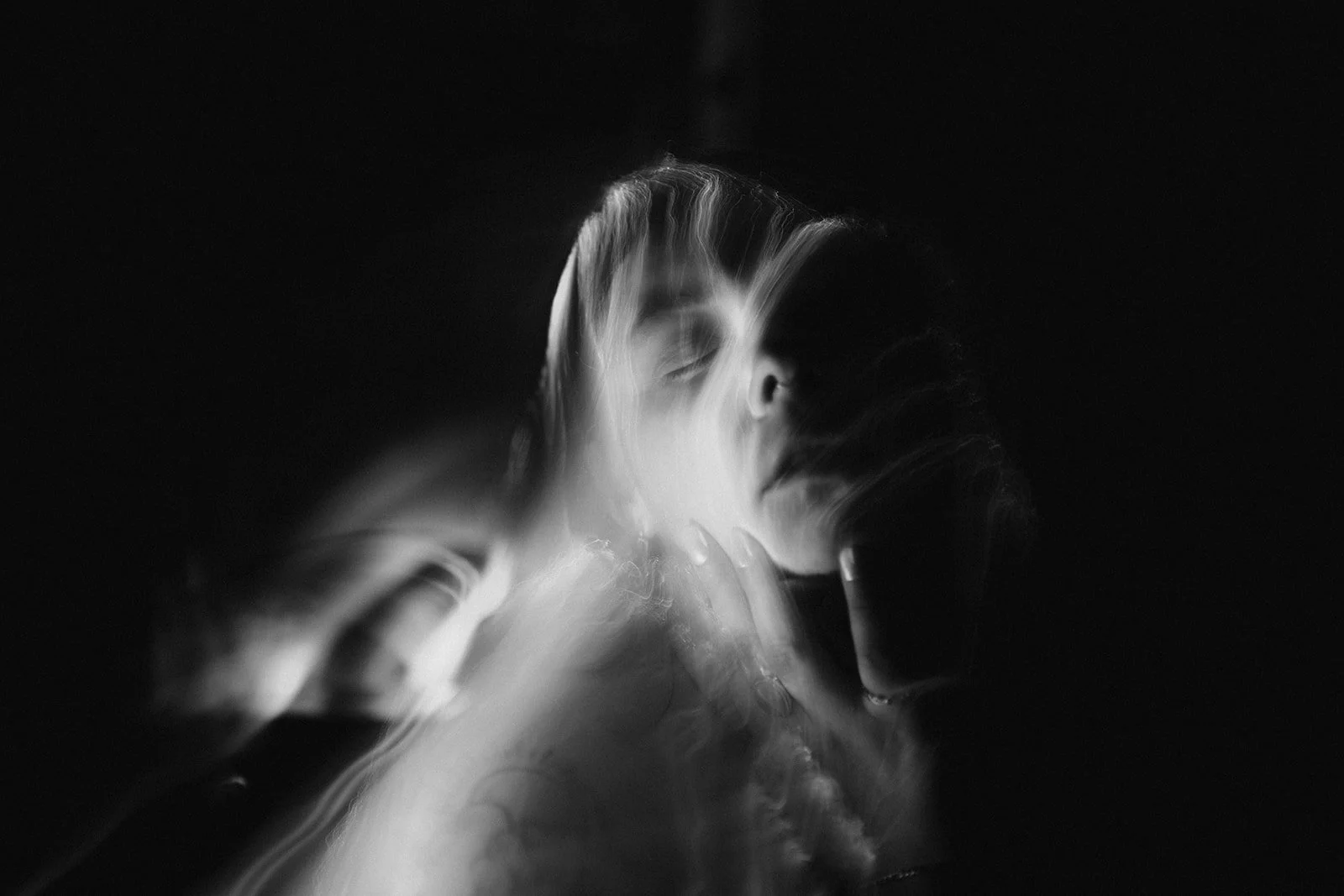 Abstract black and white portrait photograph with blurred motion effect, showing a woman's face and hands.