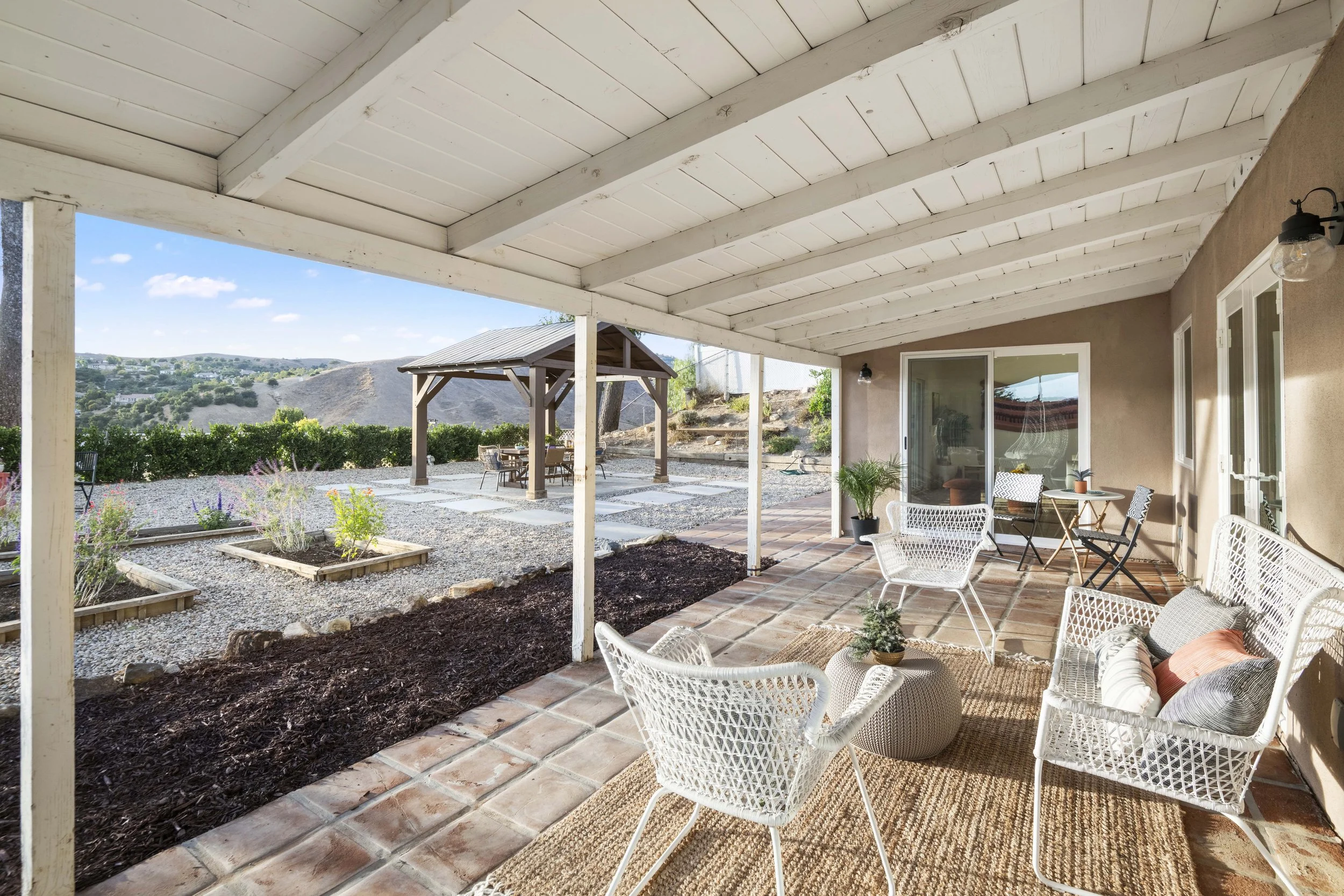 Covered Los Angeles patio with white wicker seating and garden view — affordable outdoor listing photo by Intuition Real Estate Photography & Imaging.