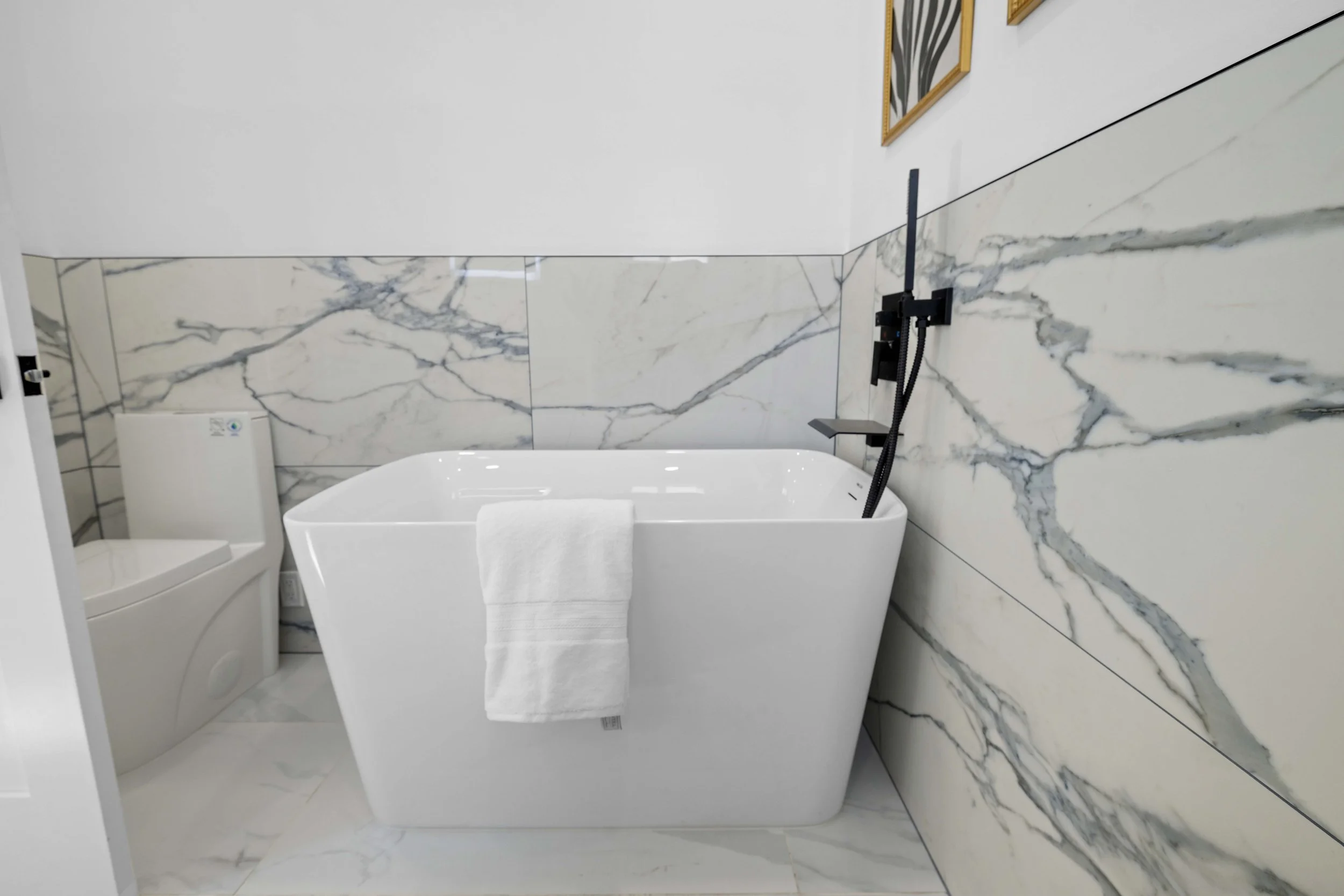 Luxury bathroom with marble walls, freestanding tub, rain shower, and black fixtures — high-end real estate photo by Intuition Real Estate Media, Los Angeles.