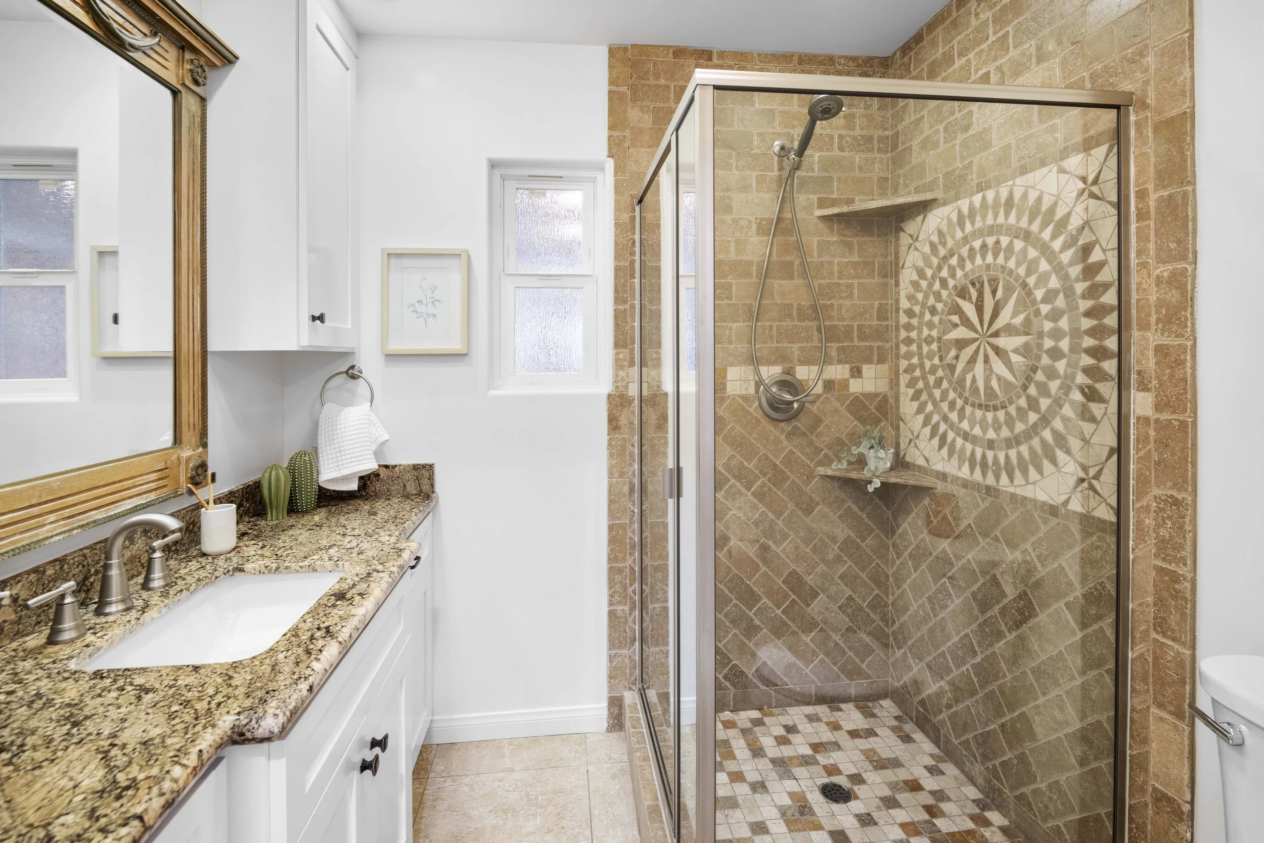 Elegant Los Angeles bathroom with mosaic-tiled shower, granite counter, and framed mirror — luxury real estate photography by Intuition Real Estate Media.