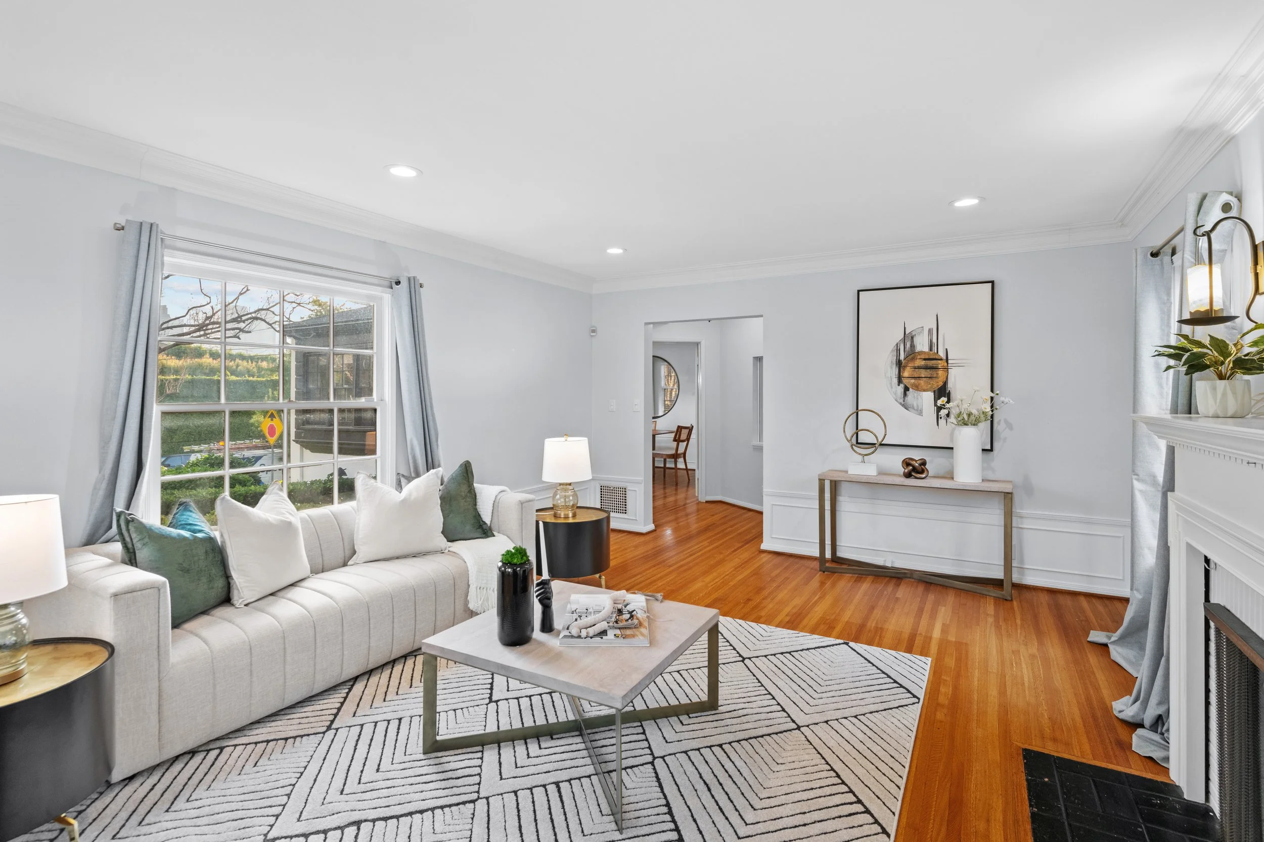 Bright Los Angeles living room with striped white sofa, blue curtains, hardwood floors, and a fireplace — interior real estate photo by Intuition Real Estate Media.