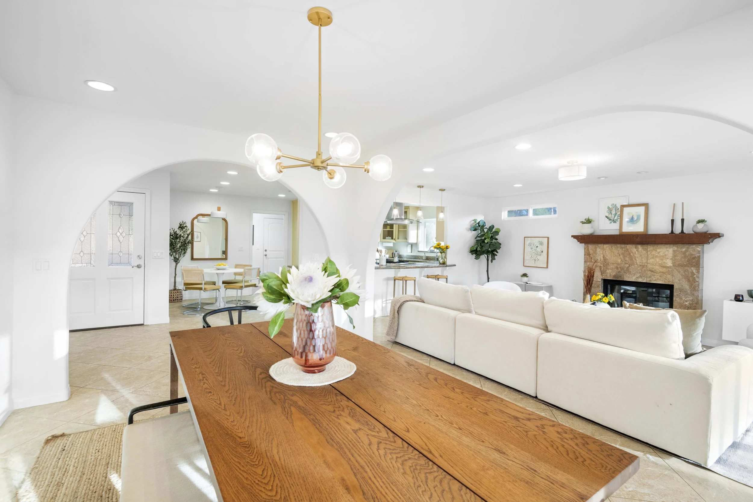 Bright LA living room with white sofa, fireplace, and kitchen view — premium real estate photo by Intuition Real Estate Photography & Imaging.