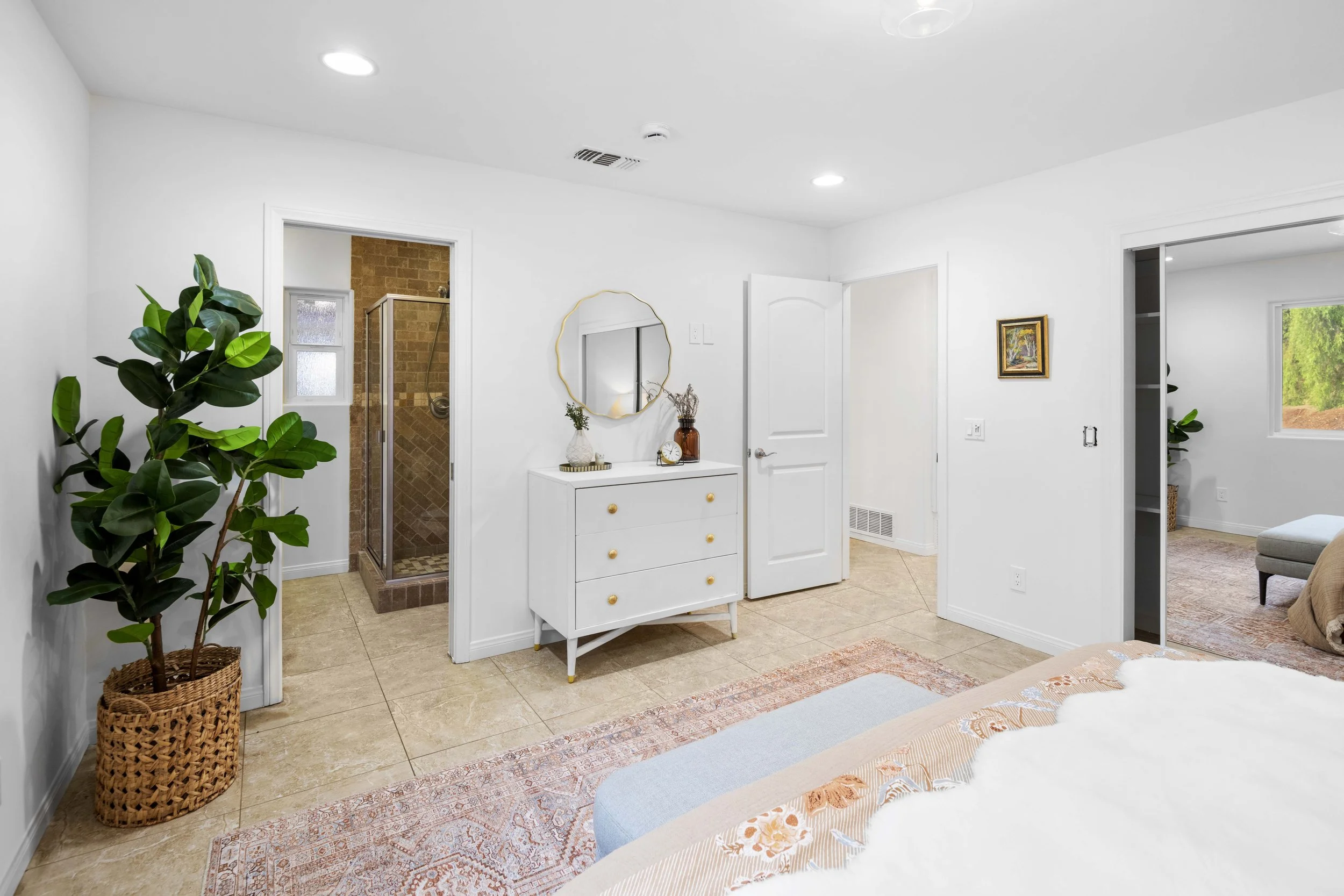 LA bedroom with white furniture, decorative vases, and view of glass-tiled shower — photographed by Intuition Real Estate Media to highlight indoor-outdoor flow.