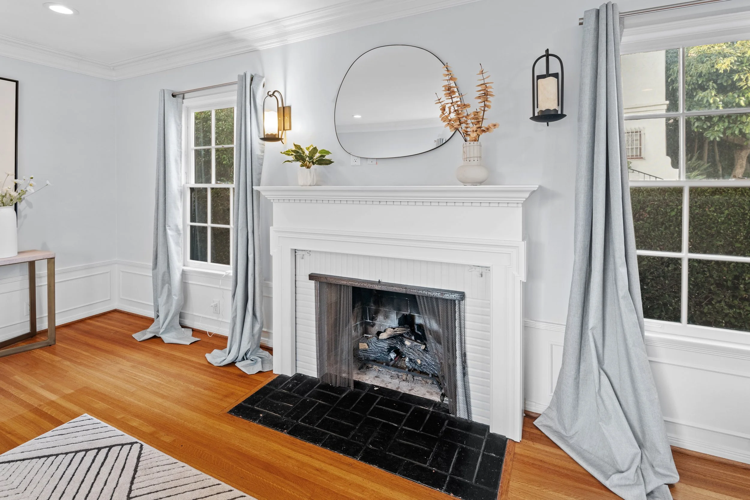Cozy LA living room with black tile fireplace, grey curtains, hardwood floors, and natural light — photographed by Intuition Real Estate Photography.